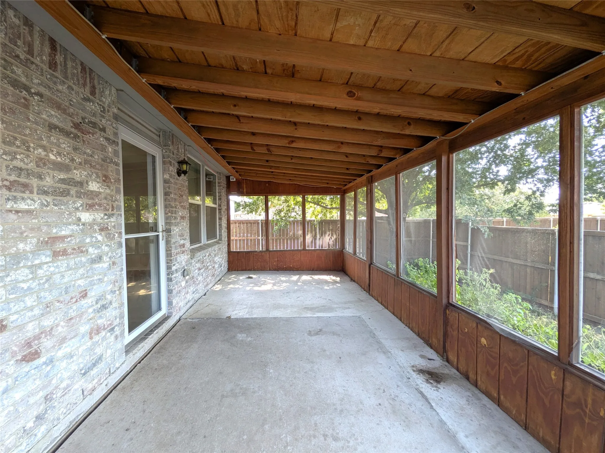 Screened porch with a wood-plank ceiling, concrete flooring, wood-paneled walls, and a brick exterior
