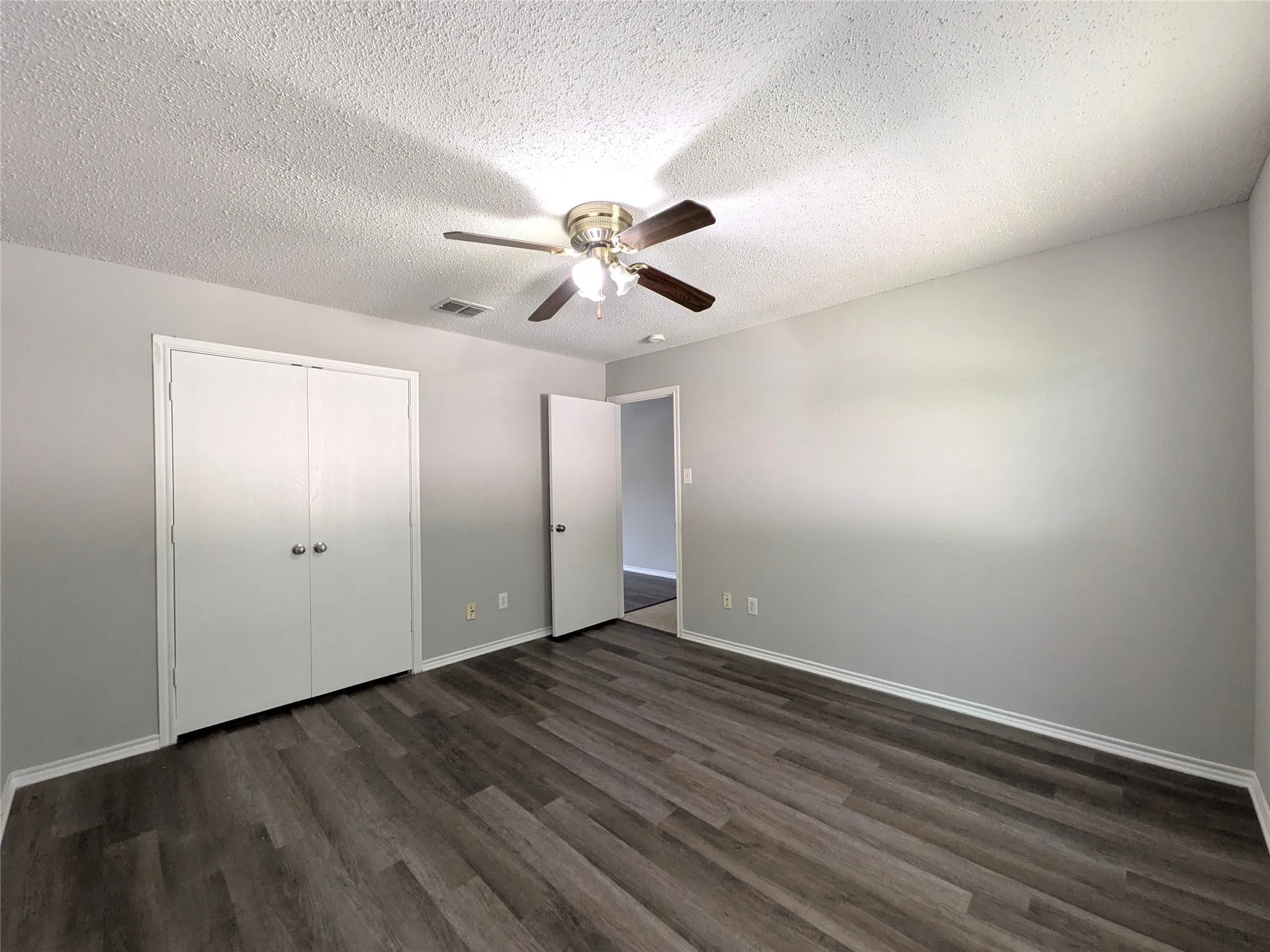 Wood-finish flooring, neutral wall tones, ceiling fan with integrated lighting, and double-door closet