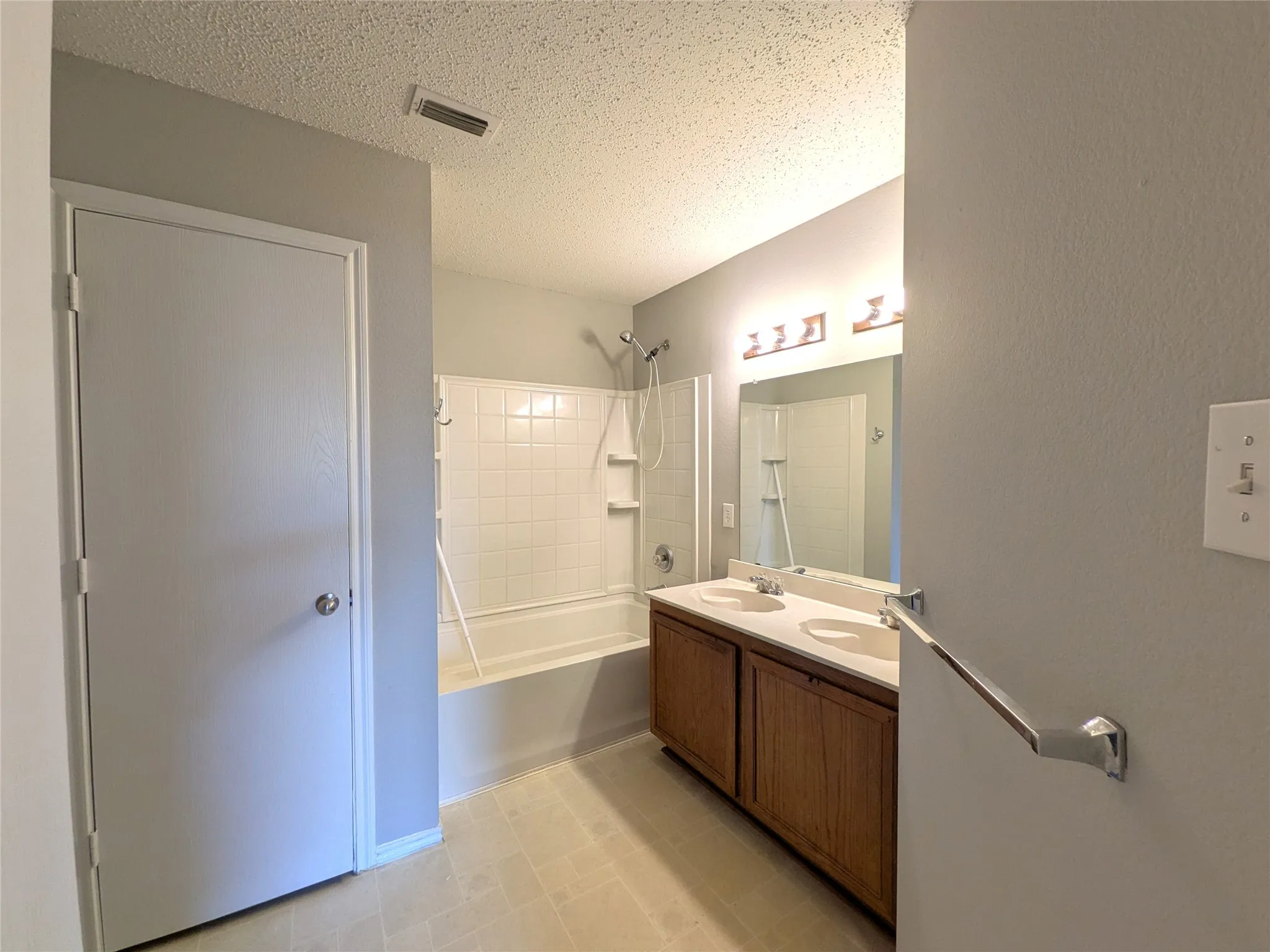 Dual sink vanity with wood-finish cabinetry, chrome fixtures, and a combined tub and shower with white tile surround