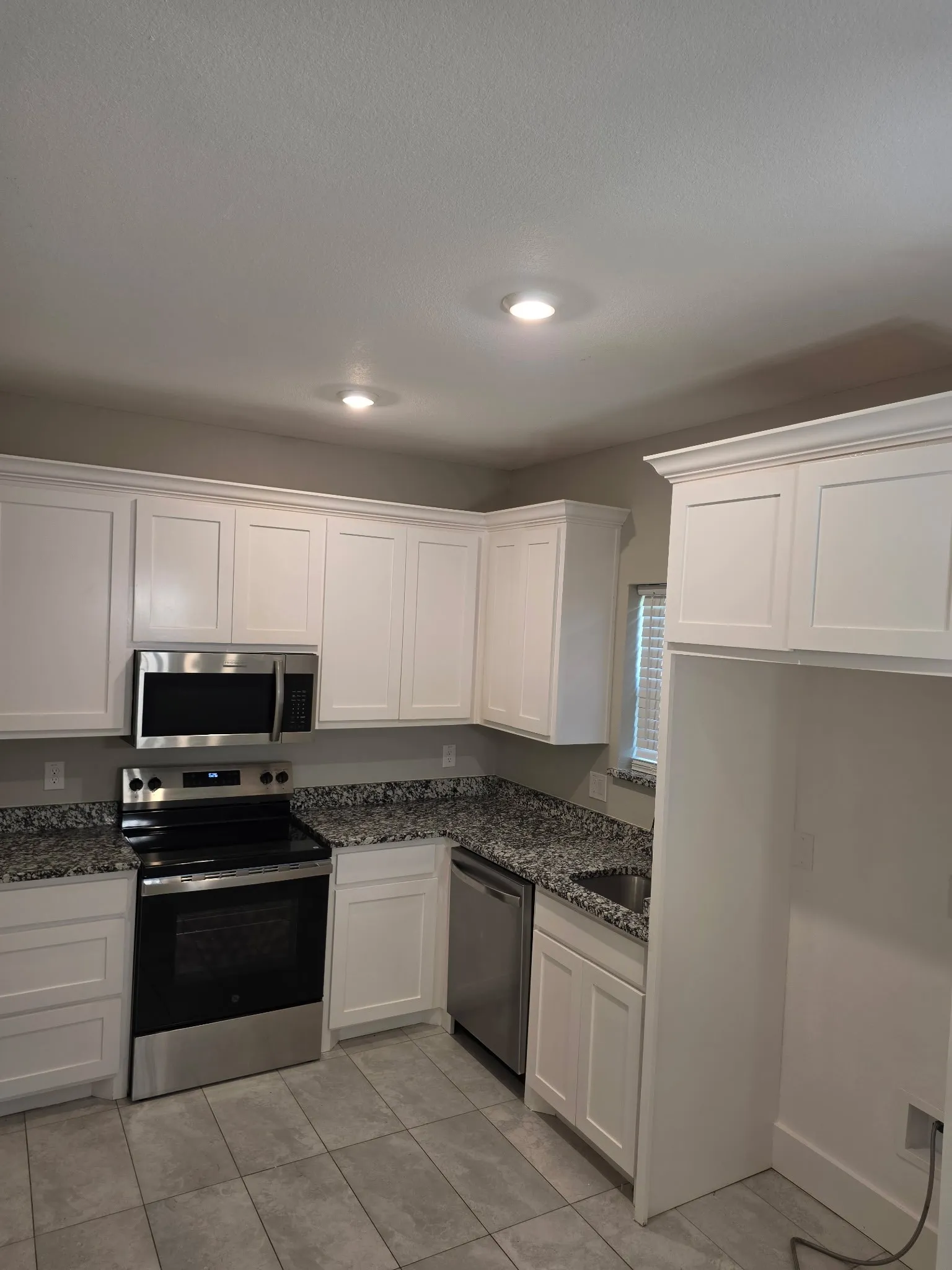 Kitchen featuring white shaker-style cabinetry, stainless steel appliances, granite-style countertops, and recessed lighting