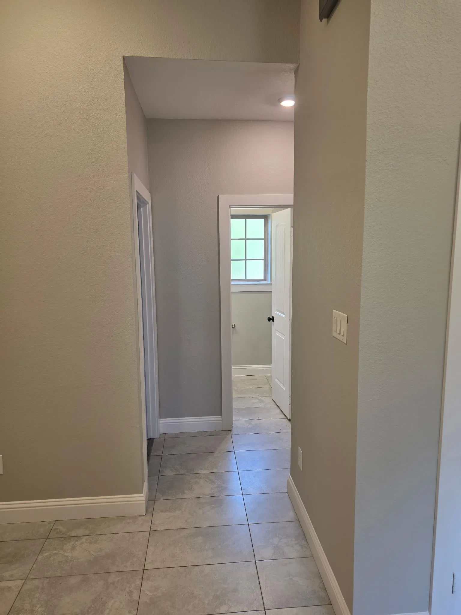Tiled flooring extending through a hallway, featuring recessed lighting and white trim