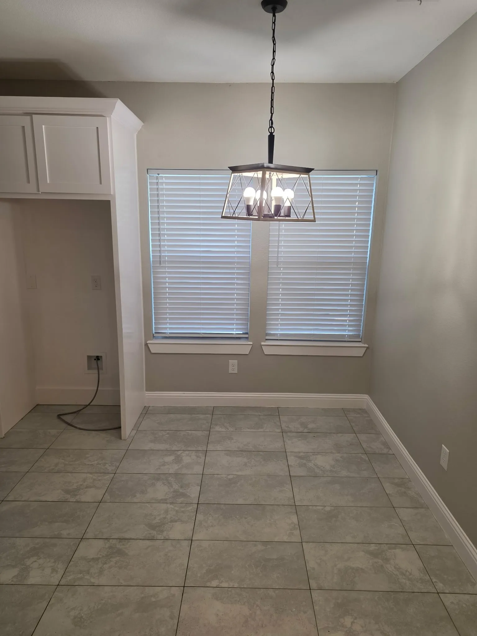 Recessed area with overhead cabinetry, two windows with blinds, a modern geometric chandelier, and tile flooring