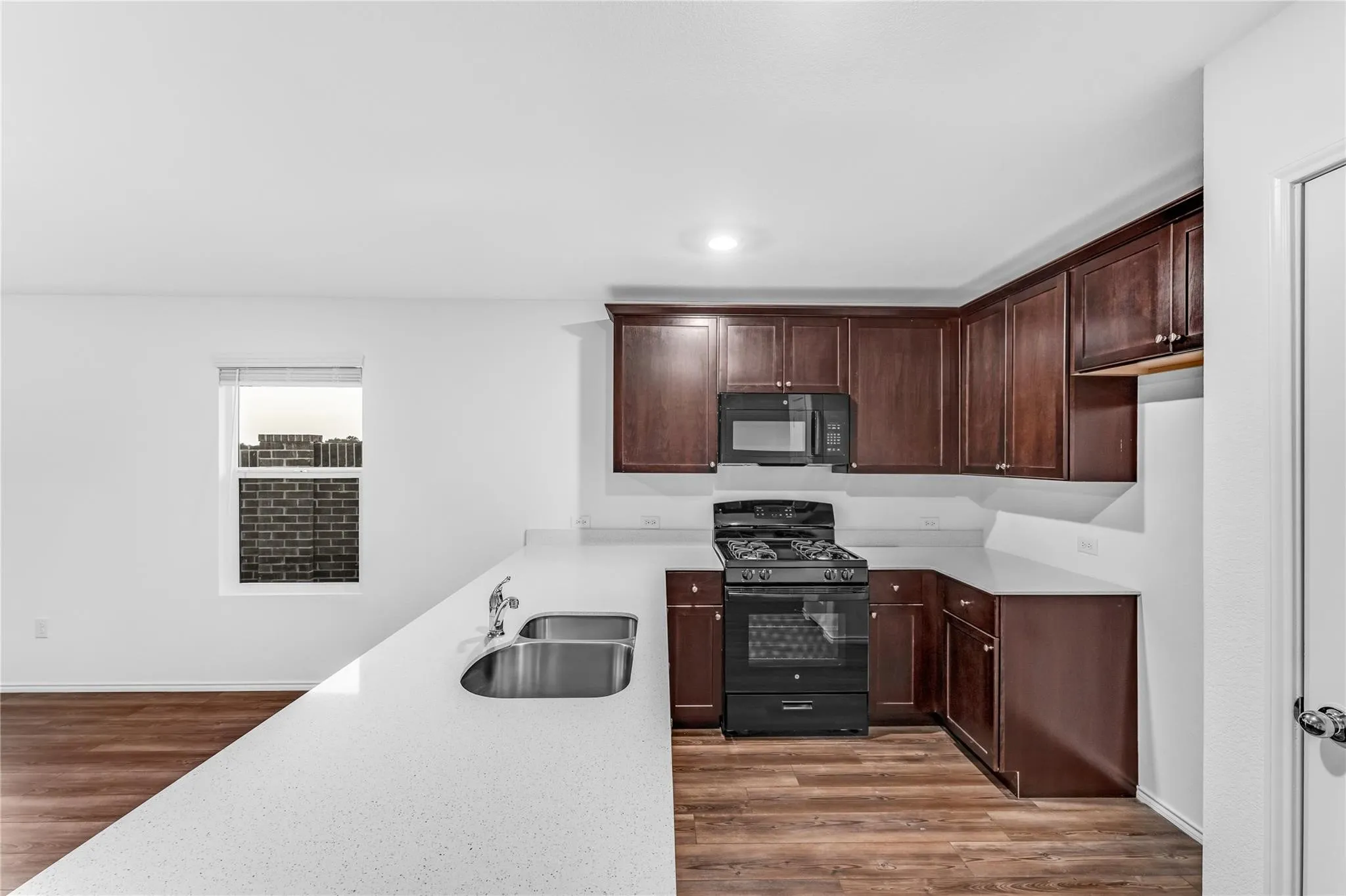 Kitchen featuring black appliances, dark wood-type flooring, dark brown cabinetry, light stone counters, and recessed lighting