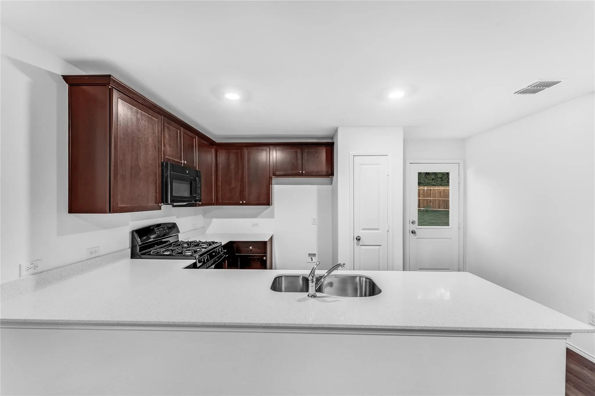 Kitchen featuring black appliances, a peninsula, dark brown cabinetry, light stone counters, and recessed lighting