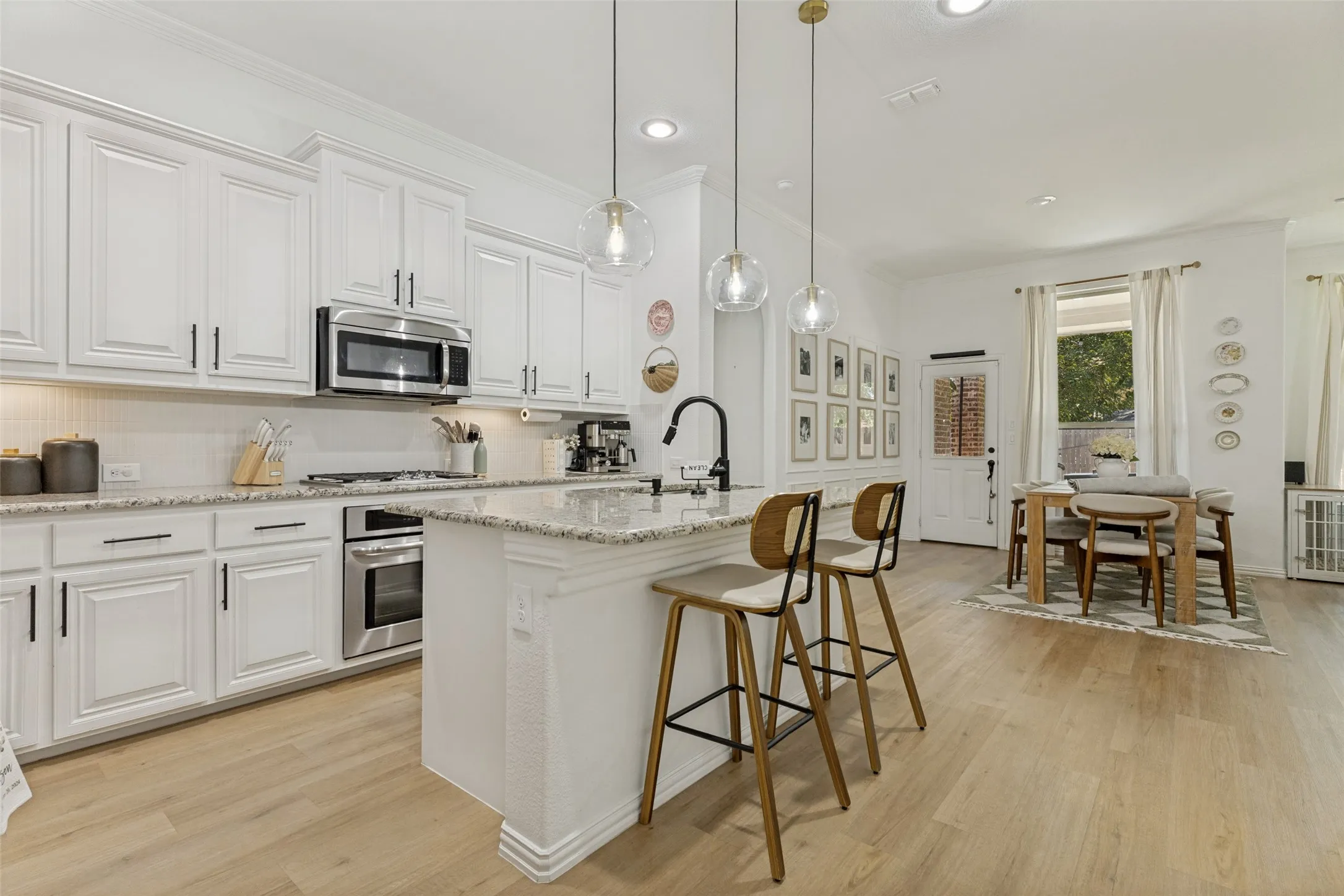 Light wood-finish flooring throughout, white shaker-style cabinetry, stainless steel appliances, granite countertops, and pendant lighting