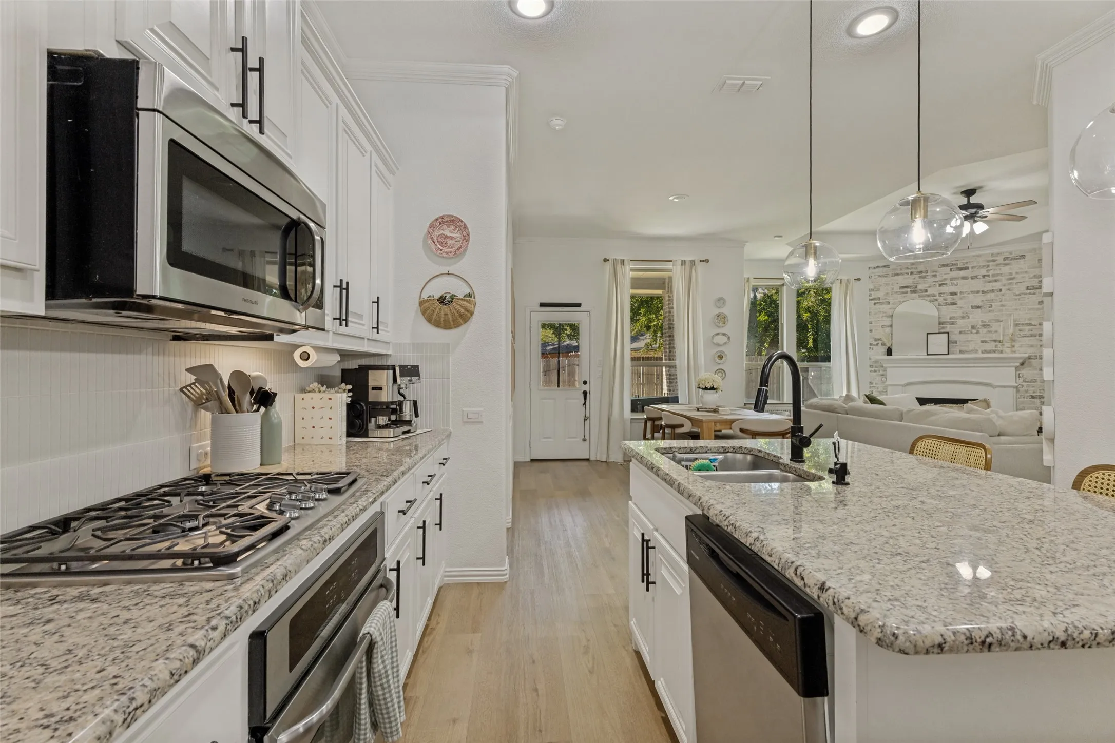 Open-concept kitchen with stainless steel appliances, granite countertops, wood-finish flooring, and white cabinetry