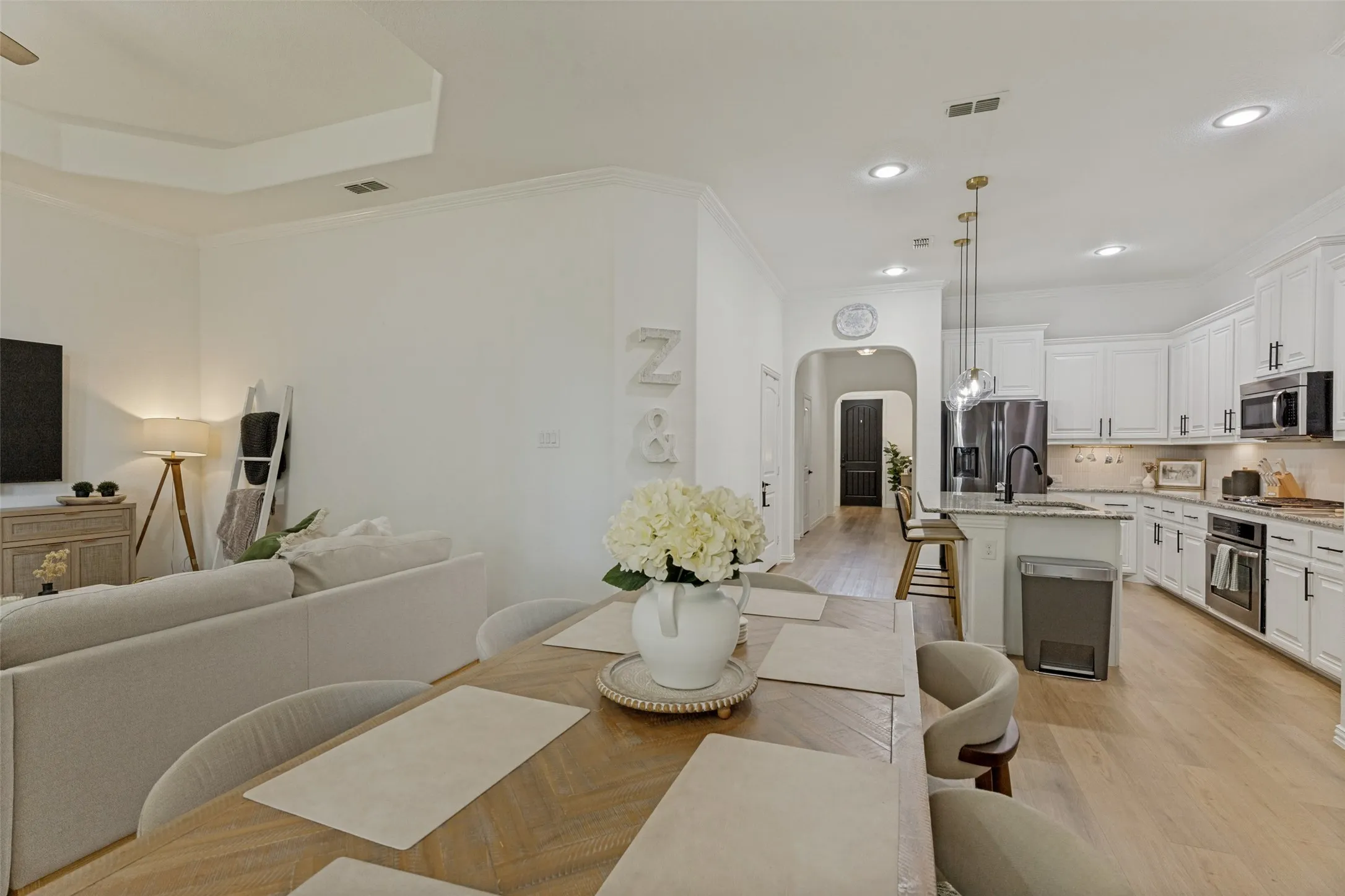 Open-concept living space featuring wood-finish flooring, recessed lighting, a tray ceiling, a kitchen with white cabinetry and dark hardware, and an island with bar seating