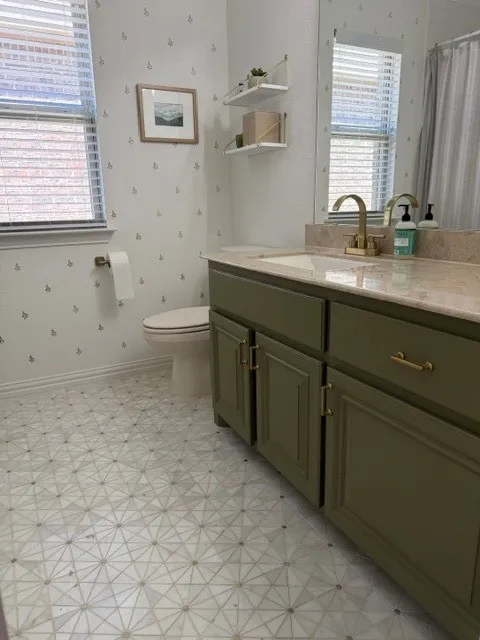 Patterned marble flooring, green vanity with gold-finish hardware, built-in sink with gold-finish faucet, stone countertop, large wall-mounted mirror