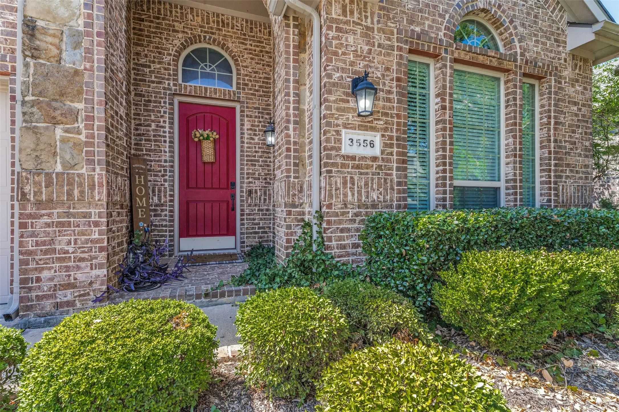 Brick exterior with stone accents, arched entryway, red paneled door, and established landscaping