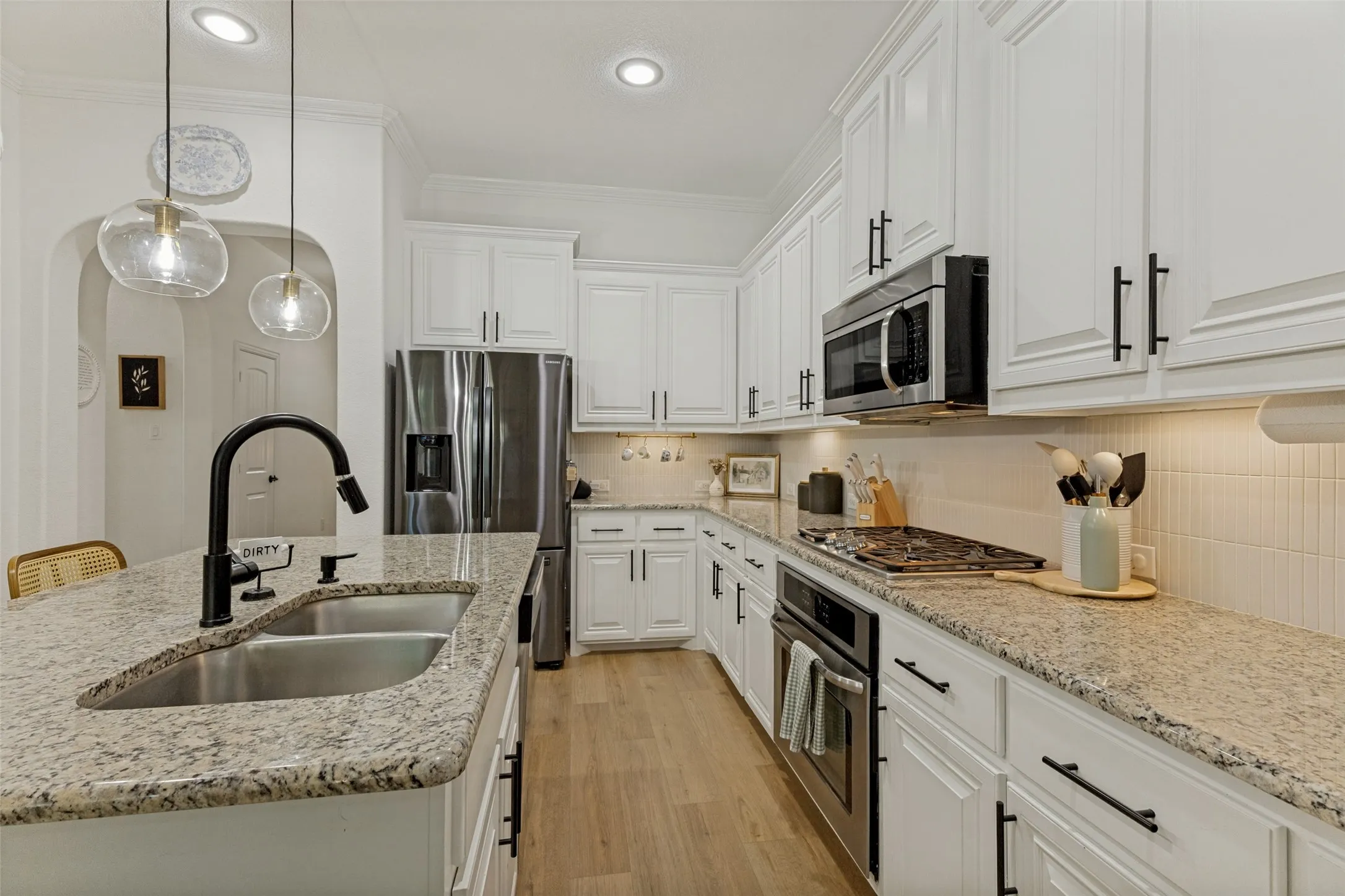 Kitchen featuring white cabinetry, granite countertops, stainless steel appliances, wood-finish flooring, and pendant lighting