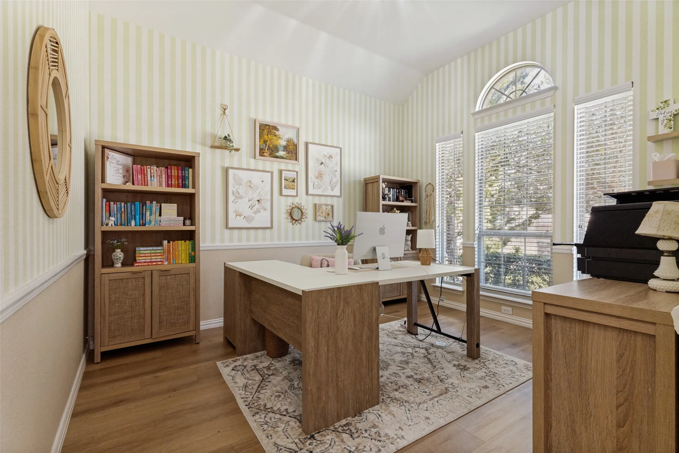 Bright home office showcasing warm wood-finish cabinetry, a spacious desk with integrated workspace, and abundant natural light from multiple large windows with transom detailing
