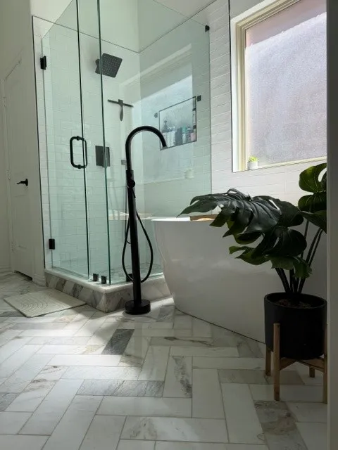 Glass-enclosed shower with matte black fixtures, freestanding soaking tub, and herringbone-patterned tile flooring