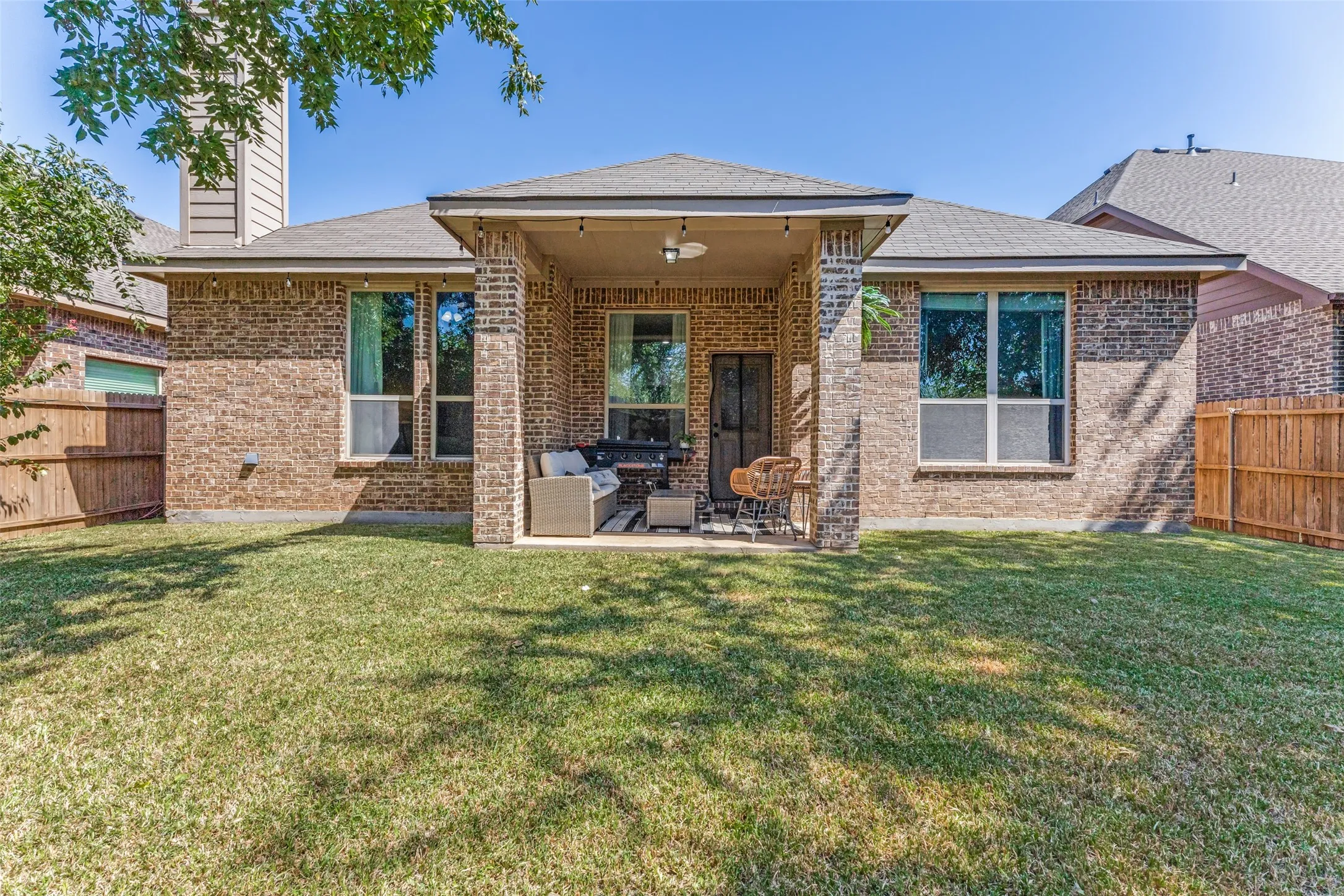 Brick exterior with a covered patio, featuring an outdoor ceiling fan, and string lighting