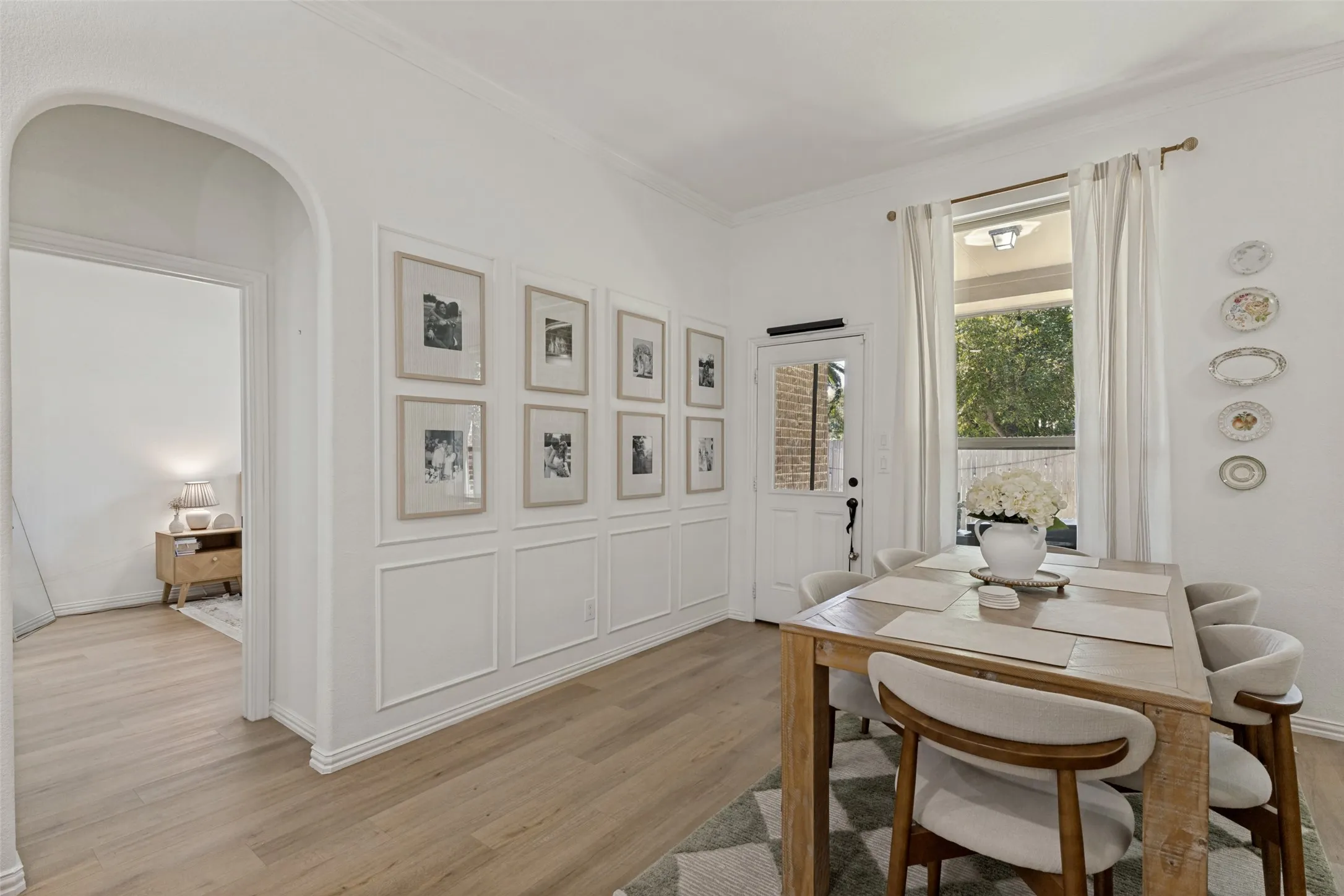 Wood-finish flooring, wainscoting with decorative trim, arched entryway, and a paneled door with glass inserts
