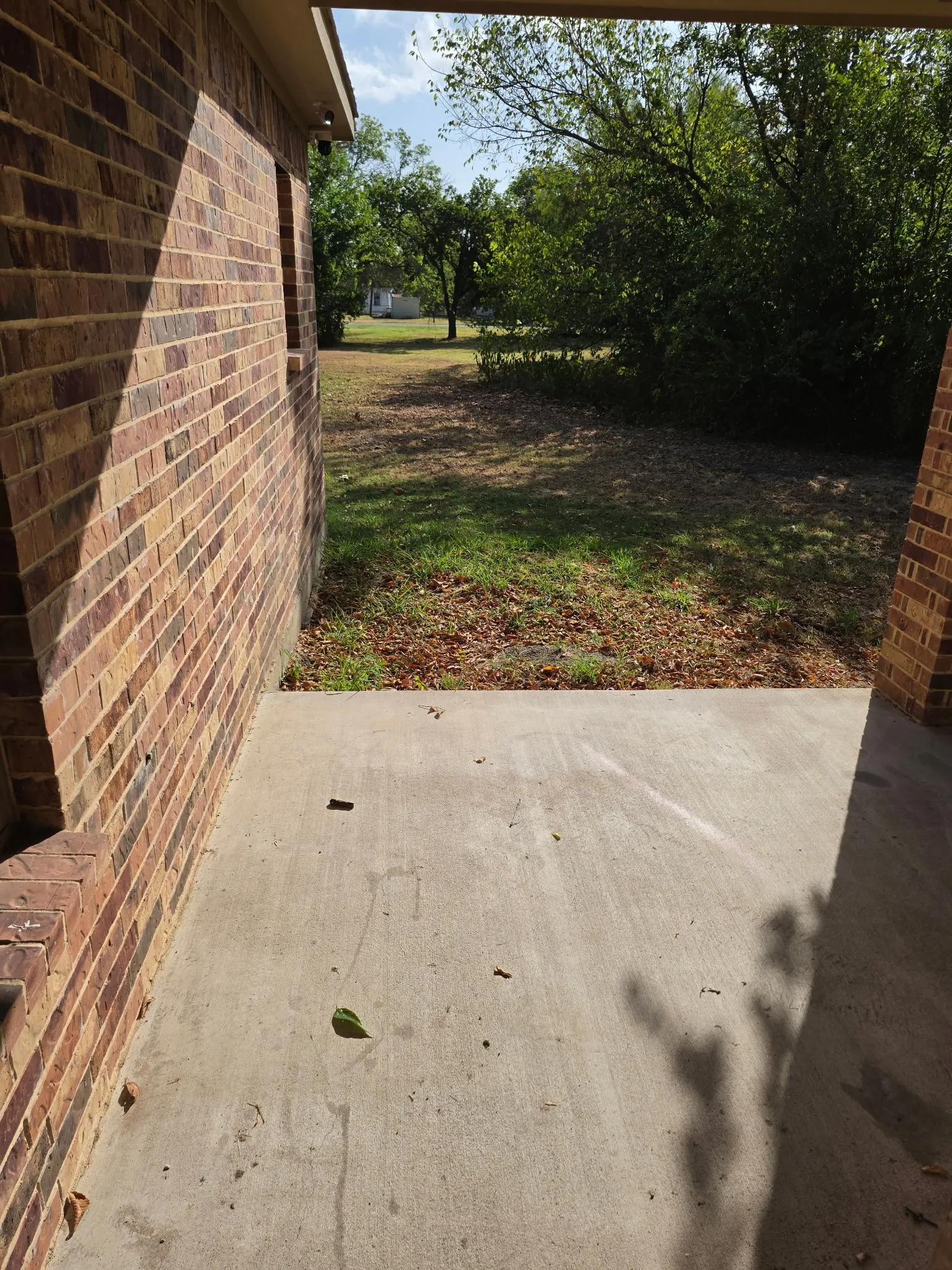Brick exterior with a covered concrete patio and mature trees