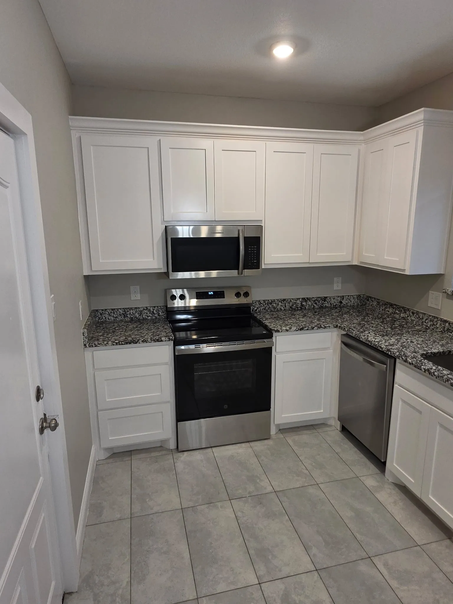 White shaker-style cabinetry, stainless steel appliances, speckled stone countertops, and gray tile flooring