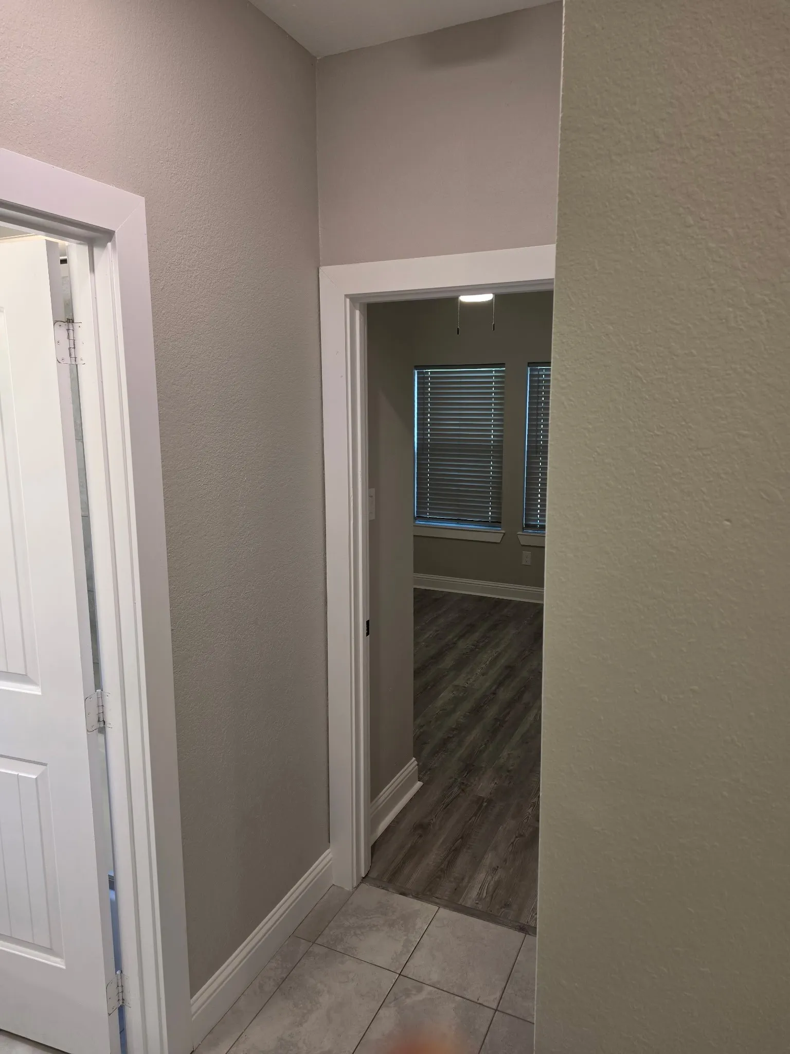 Hallway with tile flooring, neutral wall paint, white trim, and a paneled door
