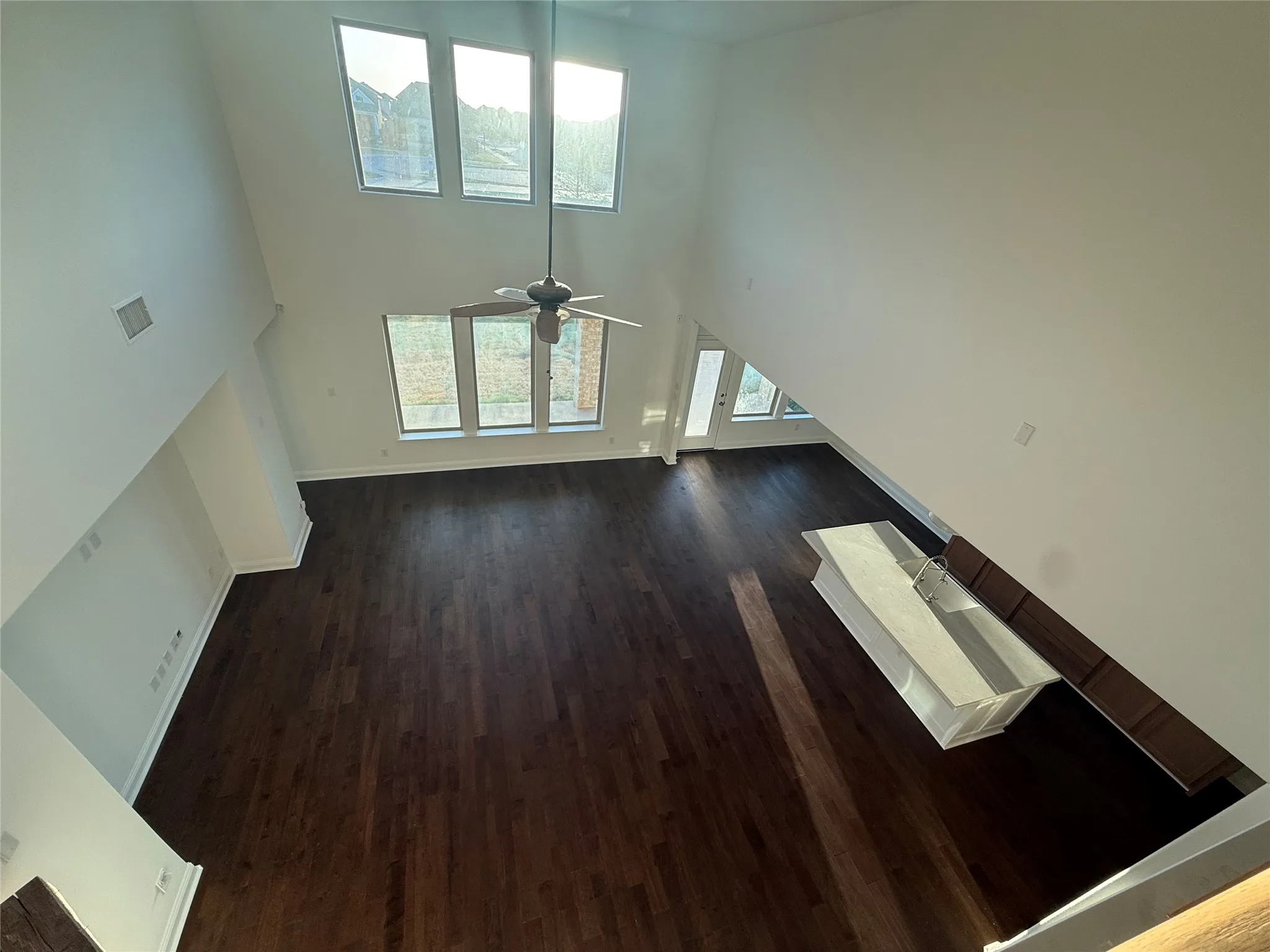 Expansive living area with double-height ceilings, dark wood-finish flooring, a contemporary ceiling fan, and multiple large windows