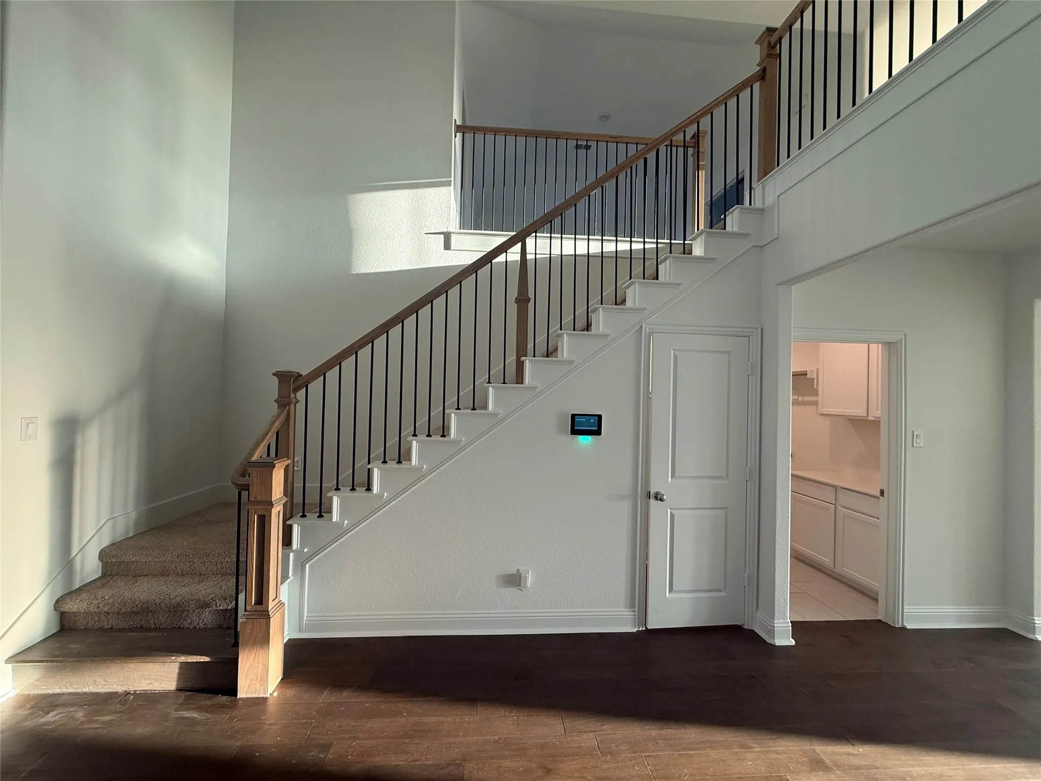 Two-story foyer with wood-finish flooring, staircase with wood handrail and wrought iron balusters, and white paneled doors