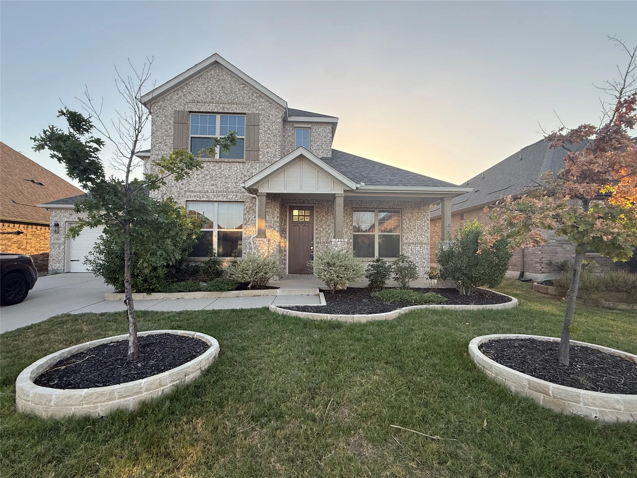 Brick façade with stone accents, covered front entry, attached garage with a concrete driveway, landscaped front yard with decorative stone edging