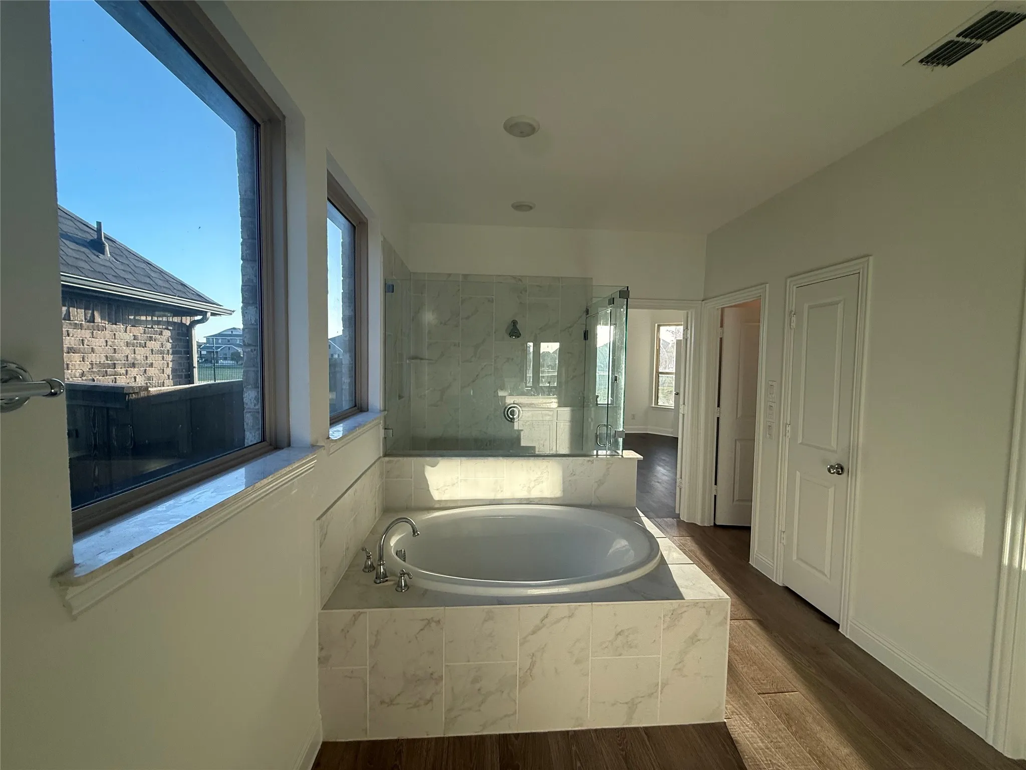 Built-in soaking tub with surrounding tile, glass-enclosed shower, wood-finish flooring, and recessed lighting