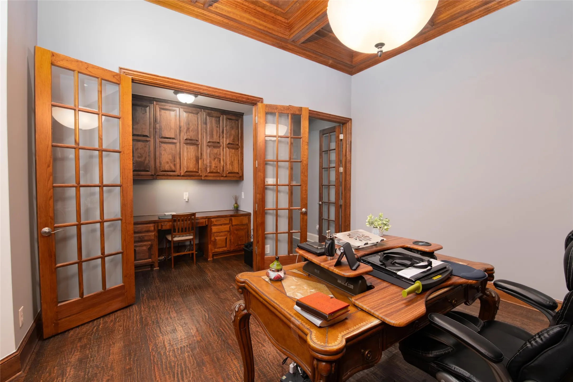 A handsome wood-accented study offers custom built-ins, glass-front cabinetry and a distinctive space for working from home.