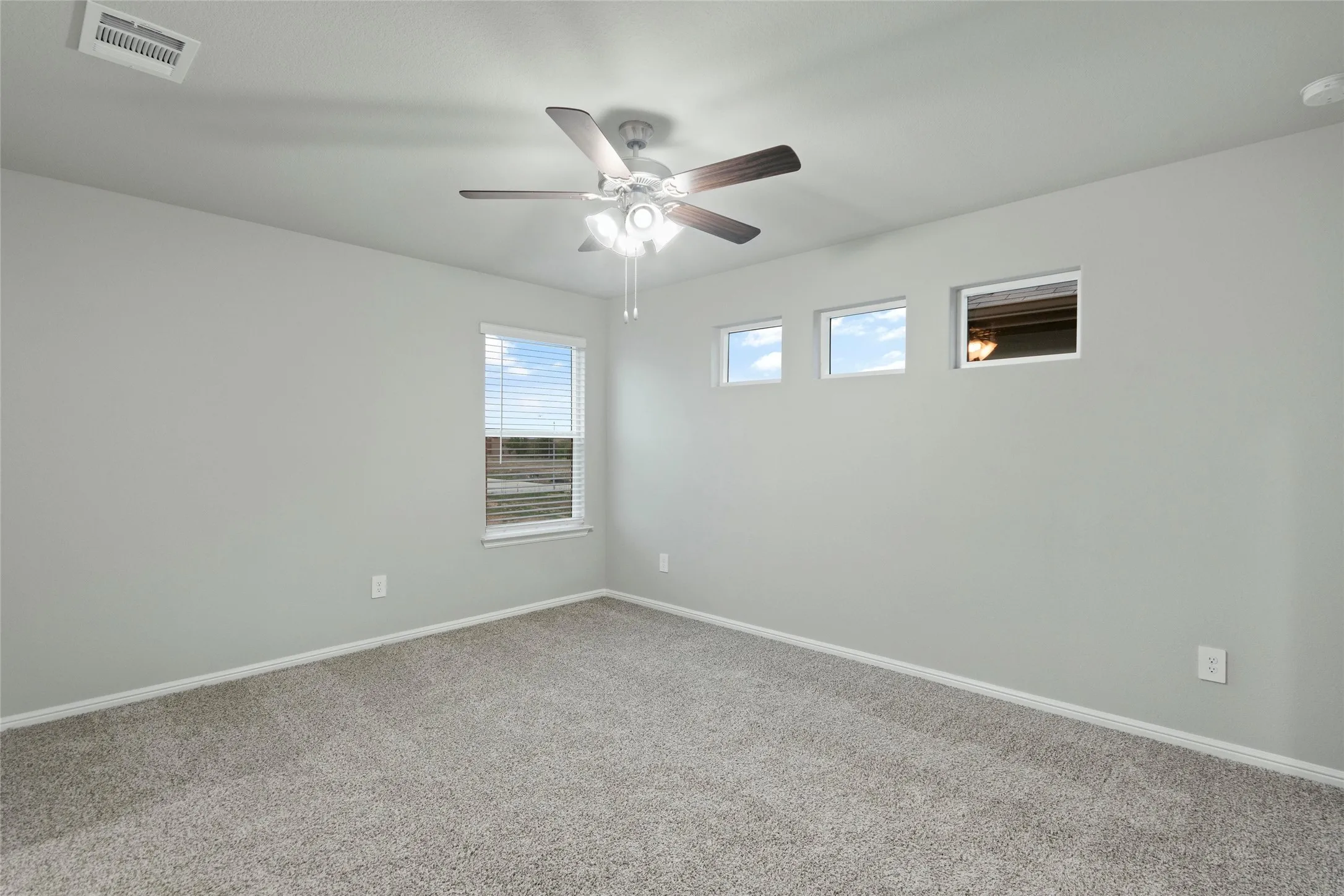 Carpeted spare room with visible vents, baseboards, and a ceiling fan