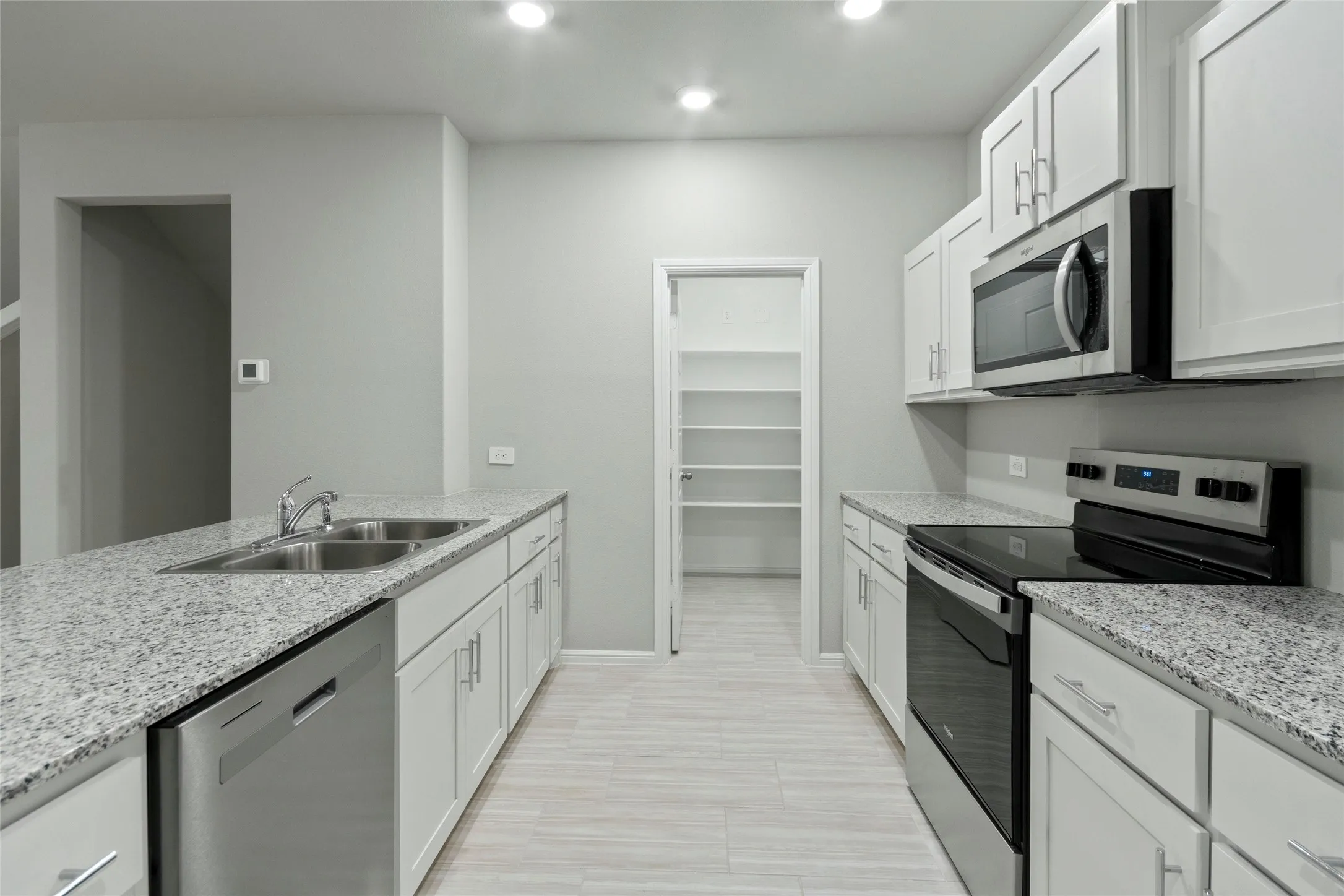 Kitchen with light stone countertops, white cabinetry, a sink, and appliances with stainless steel finishes