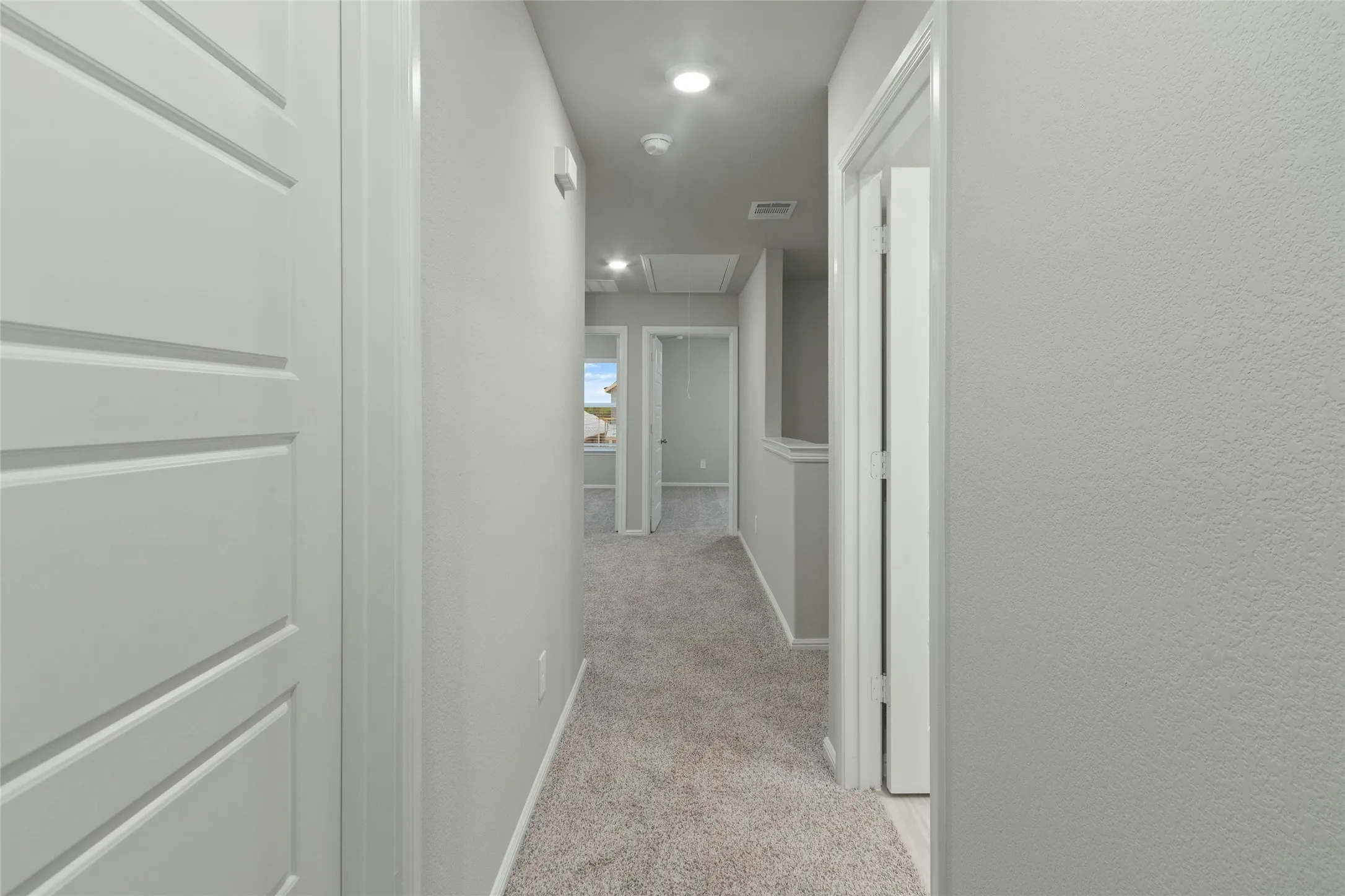 Corridor featuring baseboards, a textured wall, attic access, carpet floors, and visible vents