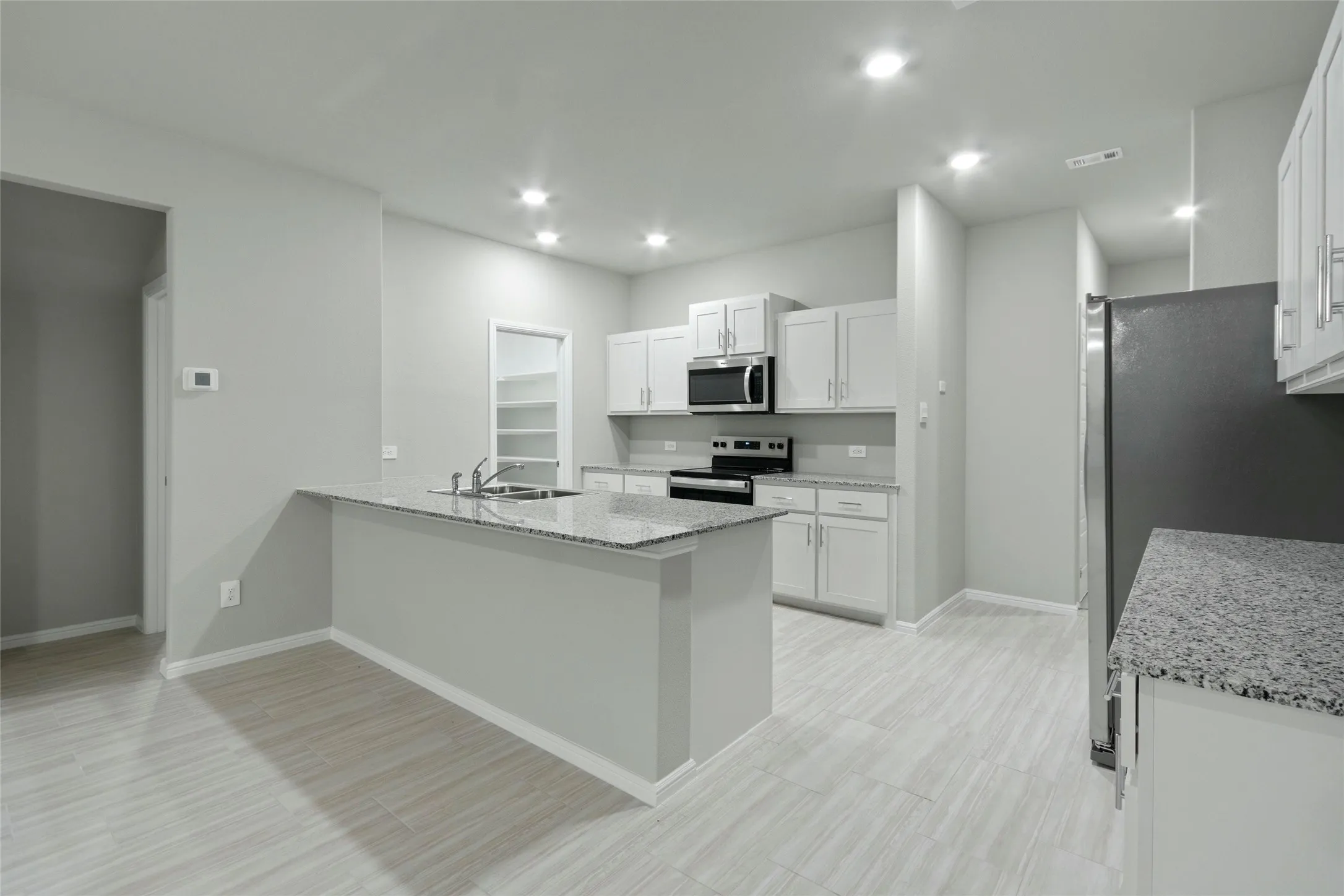 Kitchen featuring a peninsula, white cabinets, light stone counters, a sink, and stainless steel appliances