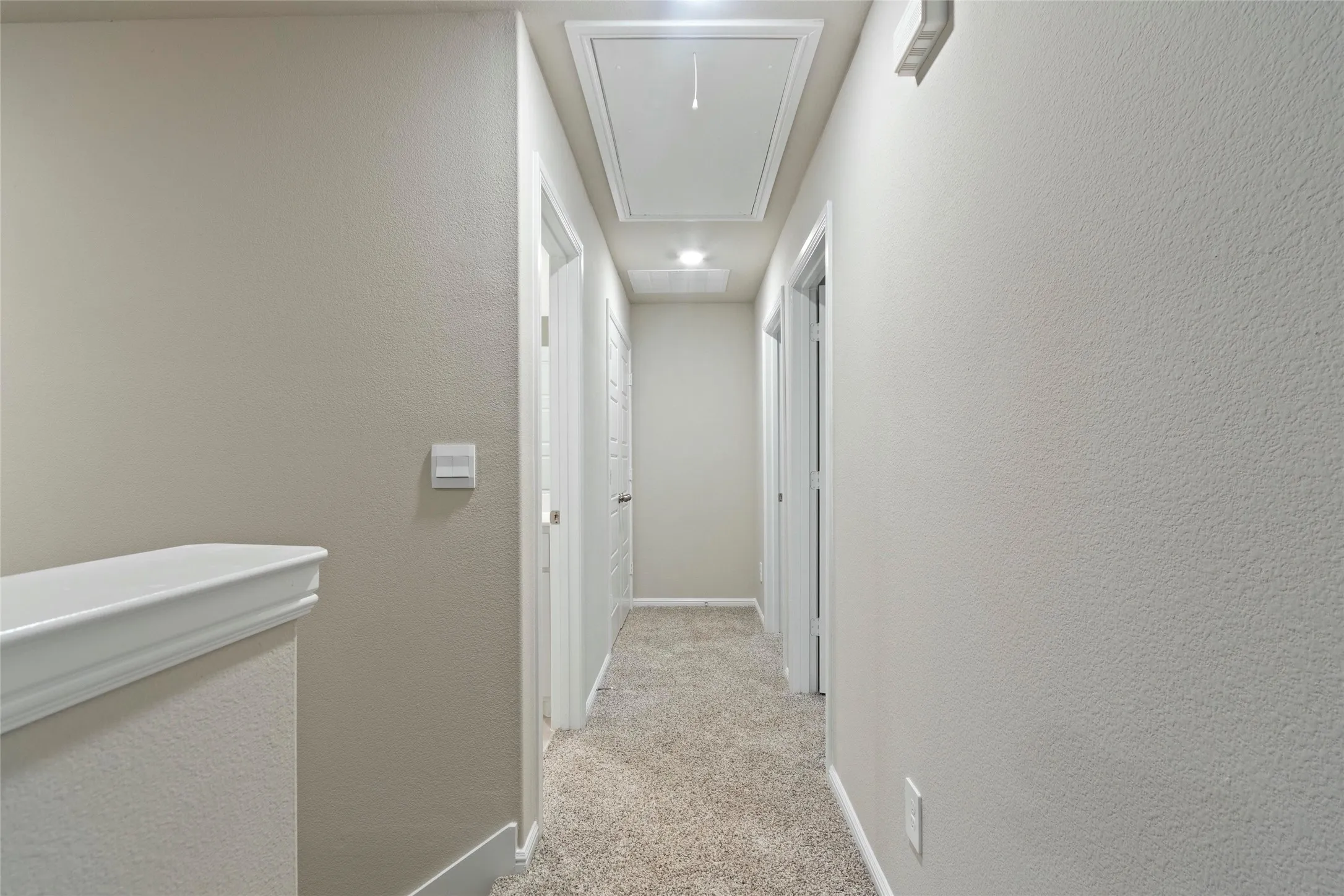 Hallway featuring light colored carpet, attic access, and baseboards
