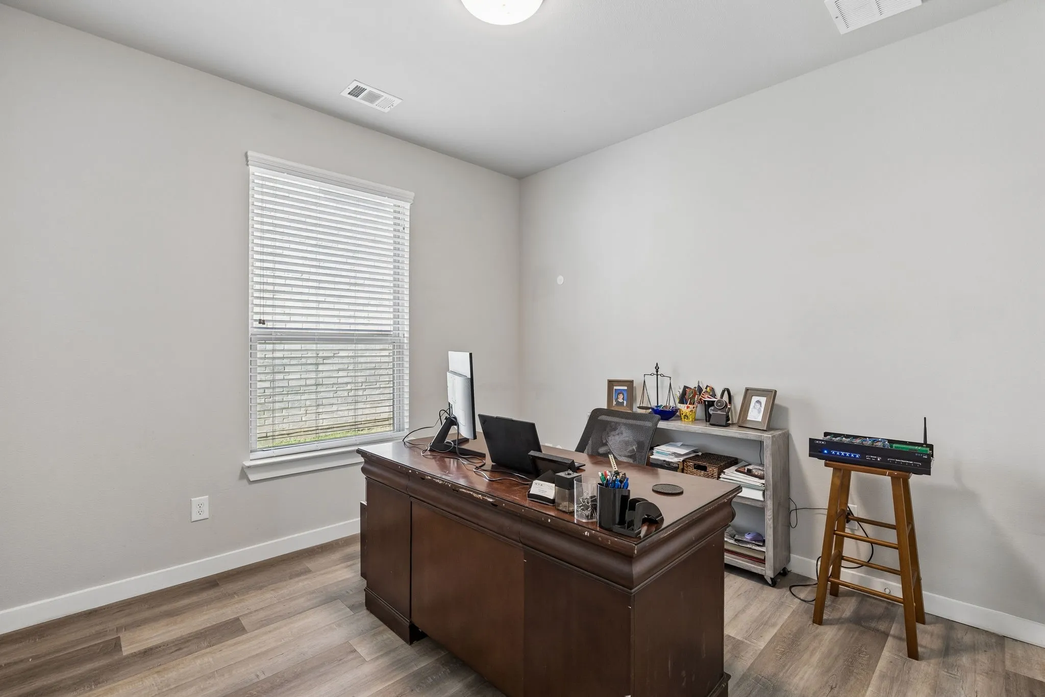 Dedicated home office featuring a spacious wood-finish desk, abundant natural light from a large multi-pane window with plantation shutters, recessed ceiling lighting, and wood-finish flooring throughout
