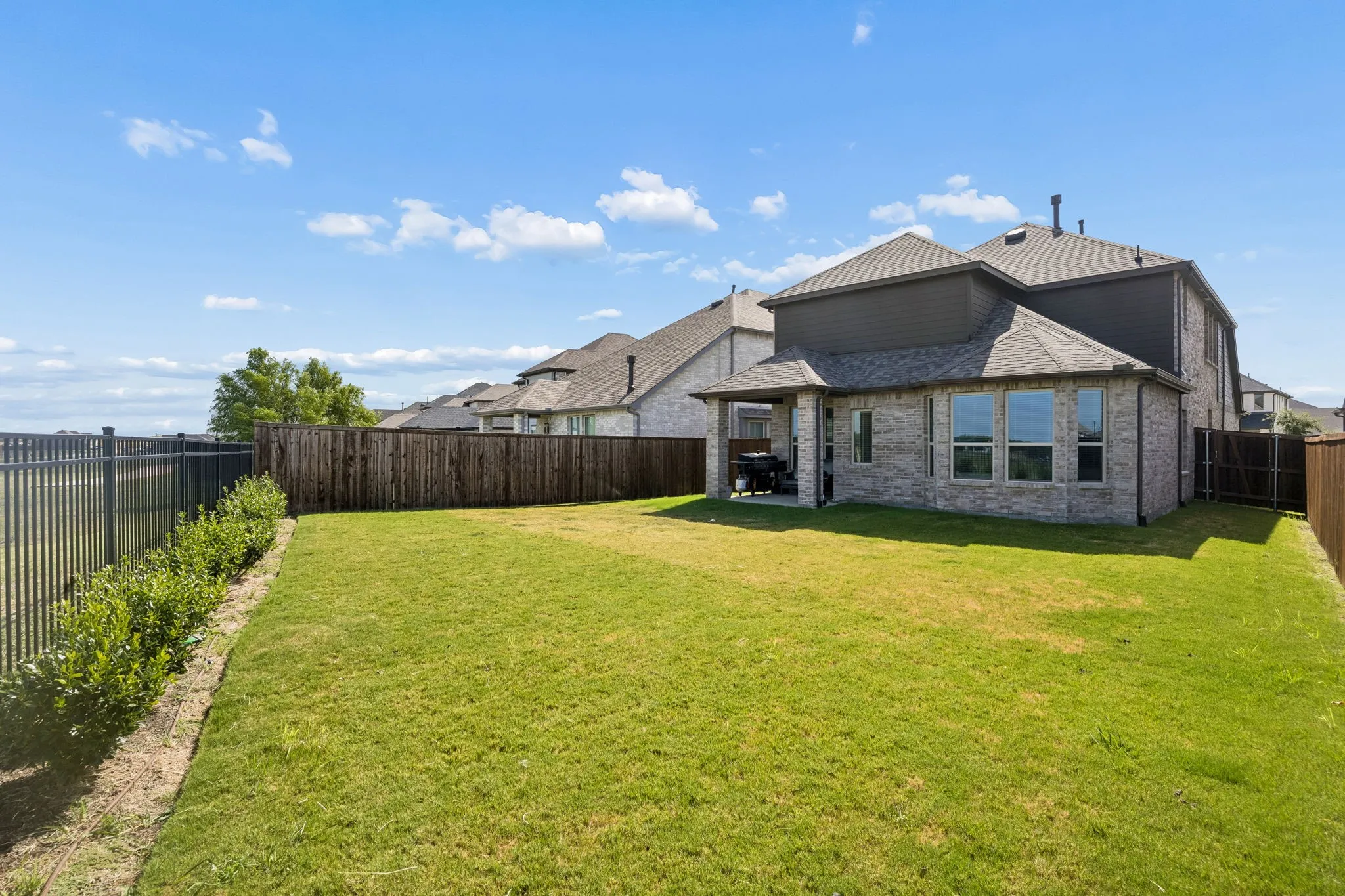 Expansive backyard featuring a manicured lawn, brick exterior, covered patio, and privacy fencing