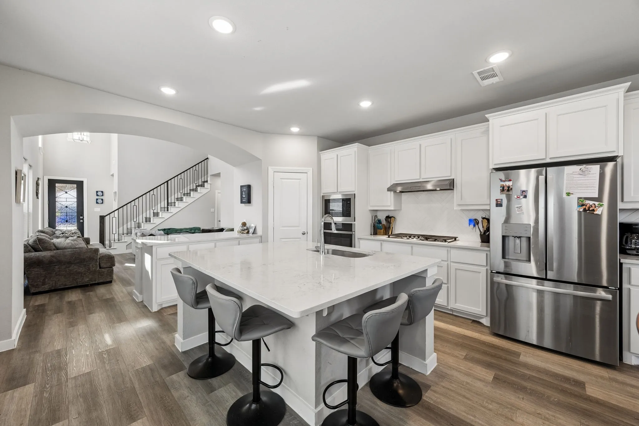 Open-concept kitchen with a large central island, white shaker cabinetry, stainless steel appliances, and wood-finish flooring