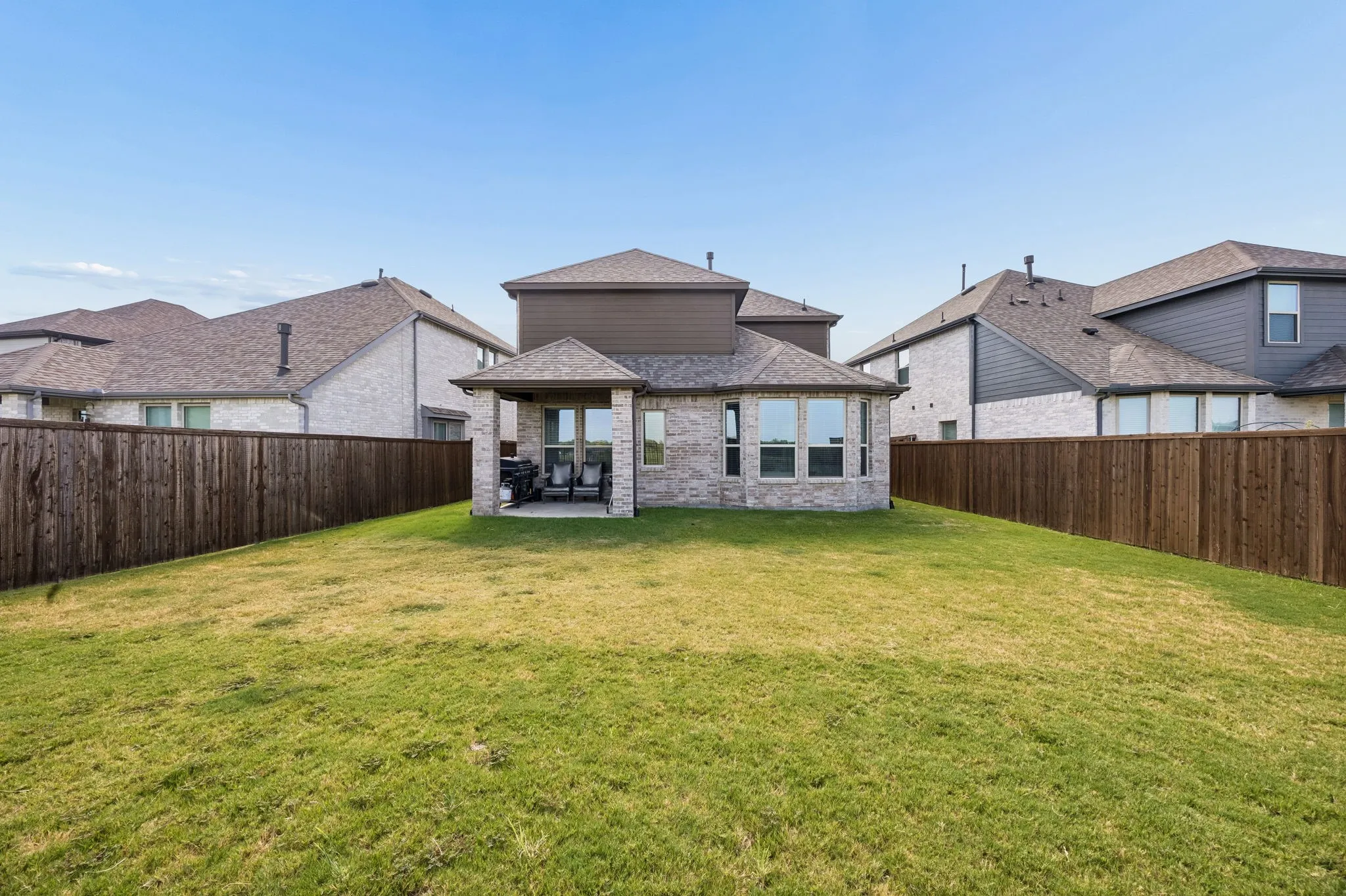 Expansive grassy yard with full privacy fencing, featuring a covered patio with a stone facade