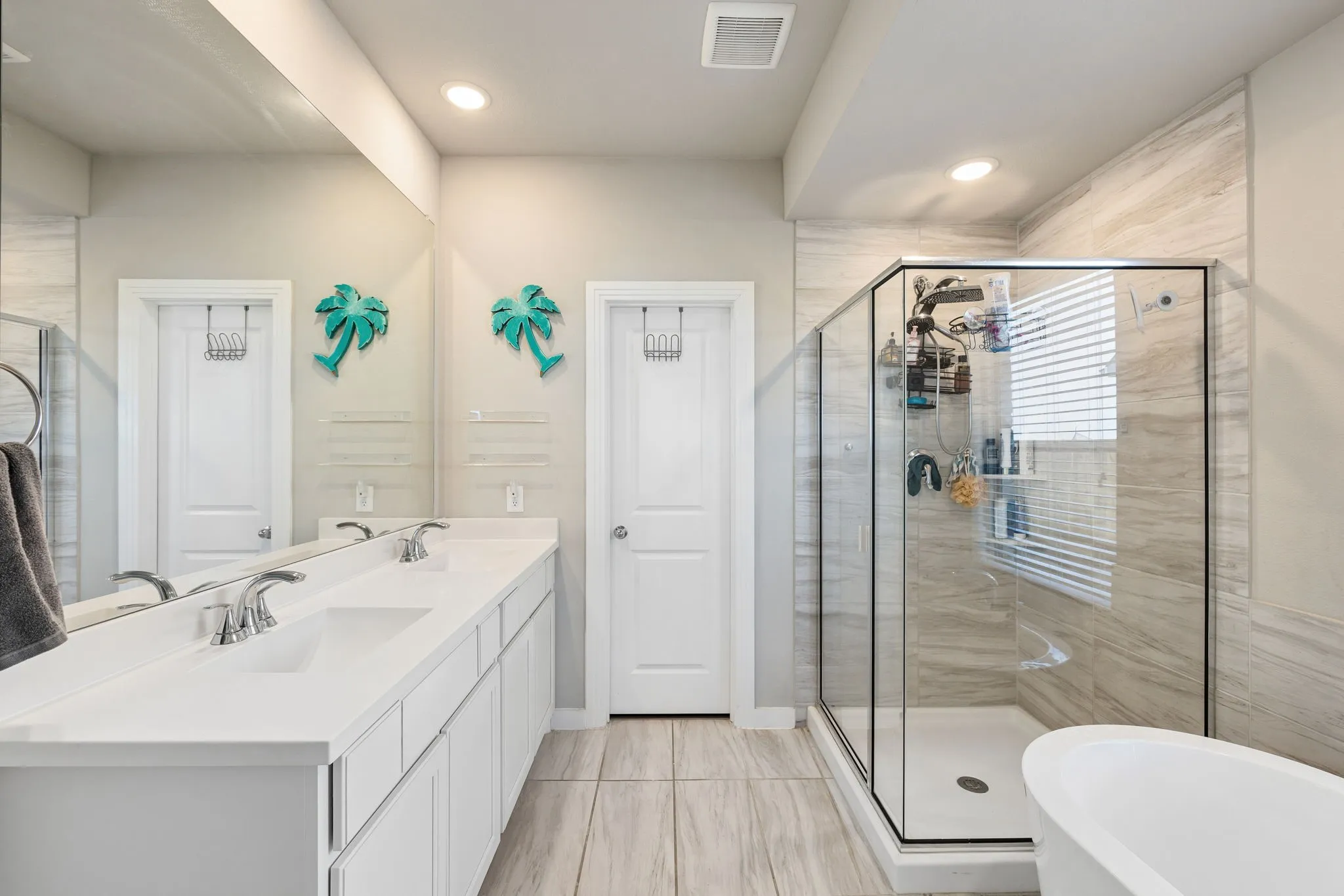 Dual sink vanity with white cabinetry, glass-enclosed shower with tile surround, freestanding bathtub, and recessed lighting