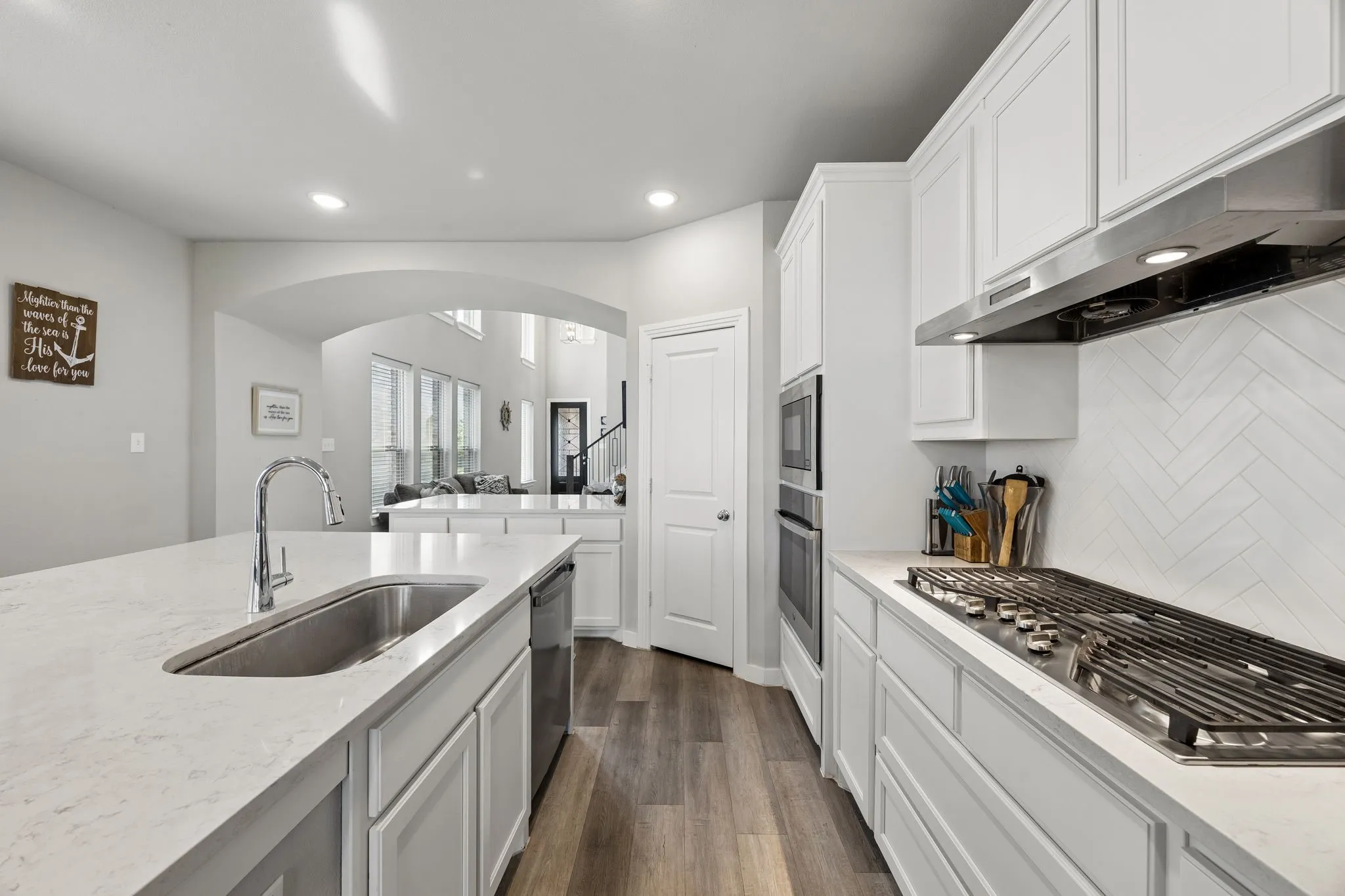 Kitchen featuring white cabinetry, light-toned countertops, a stainless steel sink, a gas cooktop, and herringbone-patterned backsplash