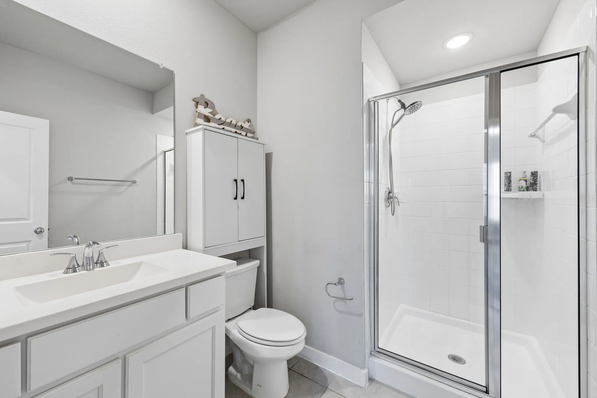 Modern primary bathroom featuring a dual-sink vanity with white cabinetry and quartz countertop, frameless glass-enclosed shower with subway tile surround and dual showerheads, white ceramic toilet, and recessed ceiling lighting throughout