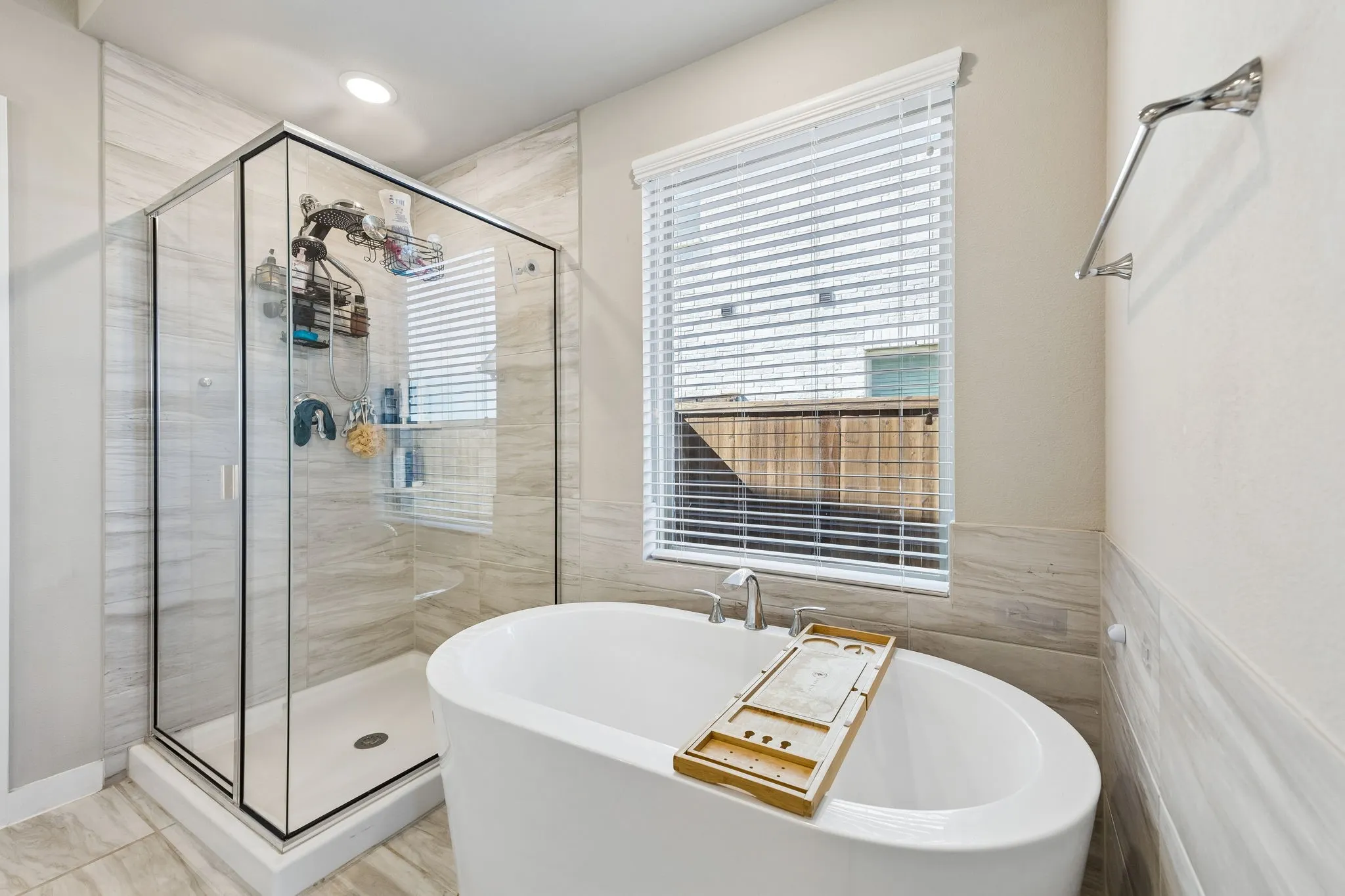 Freestanding soaking tub, glass-enclosed shower, integrated shower shelving, tiled walls, and recessed lighting