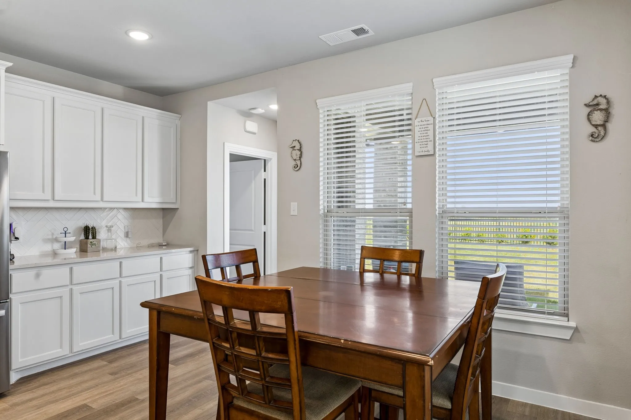 White cabinetry, chevron tile backsplash, light-toned wood-finish flooring, recessed lighting, and dual windows