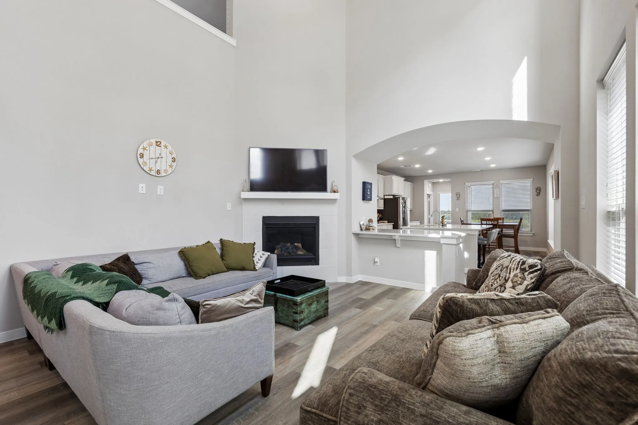 Two-story living area featuring wood-finish flooring, a contemporary fireplace with mantel, and an arched opening to the kitchen
