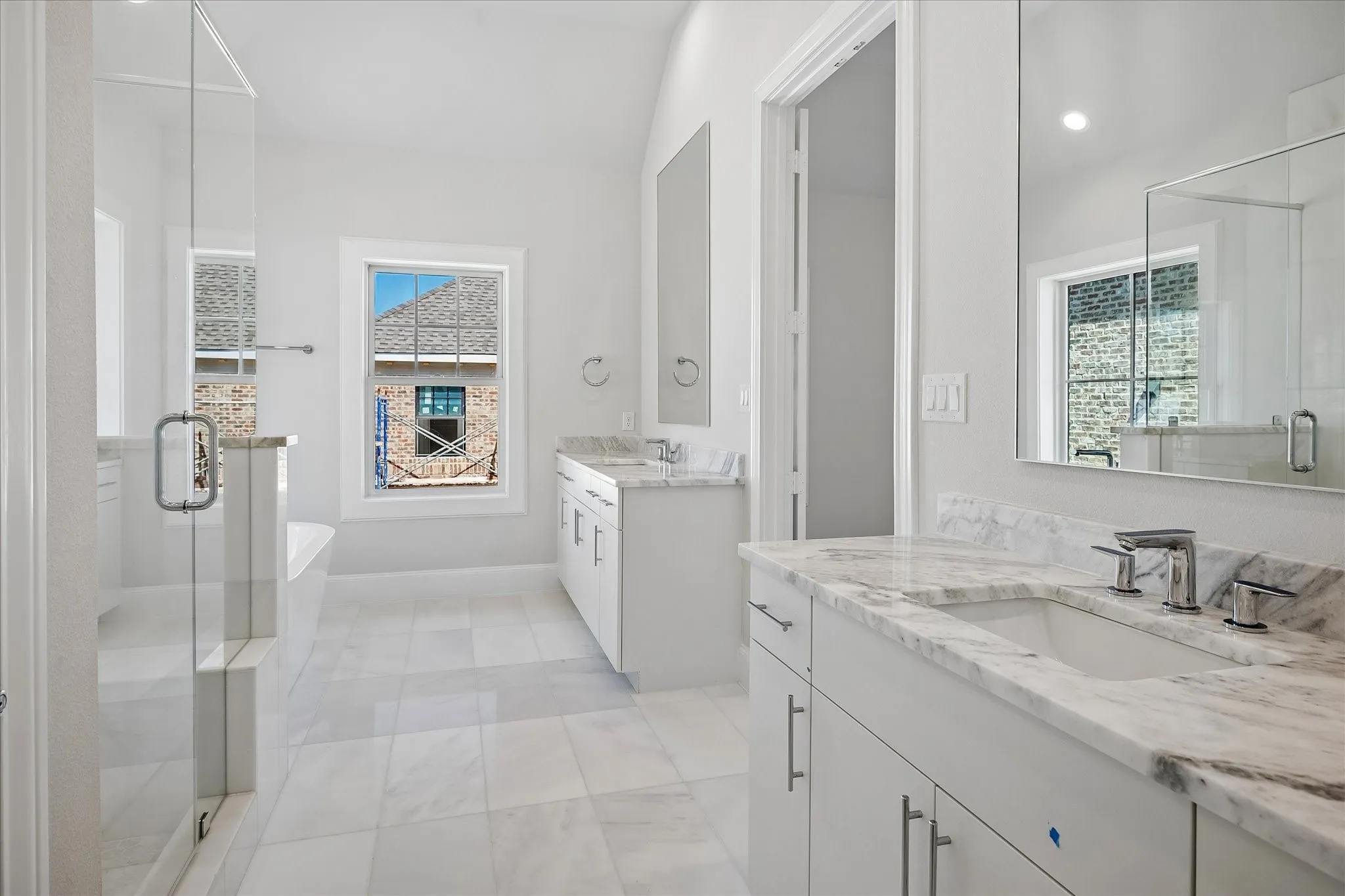 Spacious bathroom with dual vanity sinks, stone countertops, large format tile flooring, and a glass-enclosed shower