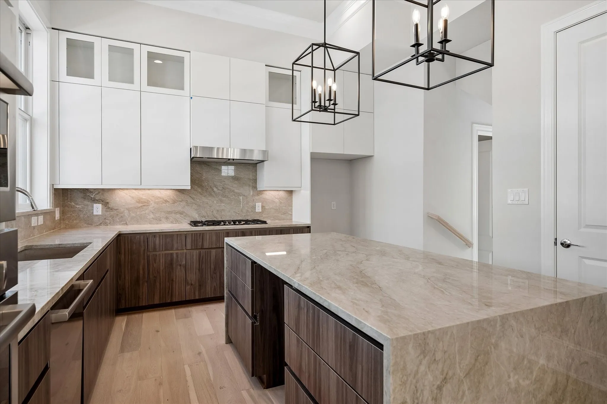 Gourmet kitchen featuring a large central island, light wood-finish flooring, integrated range hood, under-cabinet lighting, and custom cabinetry with frosted upper panels