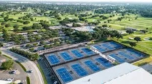 Multiple tennis courts with a surrounding fence, extensive green spaces, and mature trees