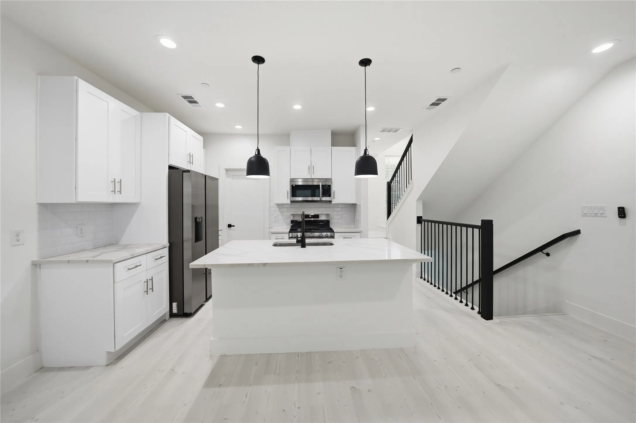 Modern kitchen featuring a large island with pendant lighting, white cabinetry, stainless steel appliances, and light wood-finish flooring