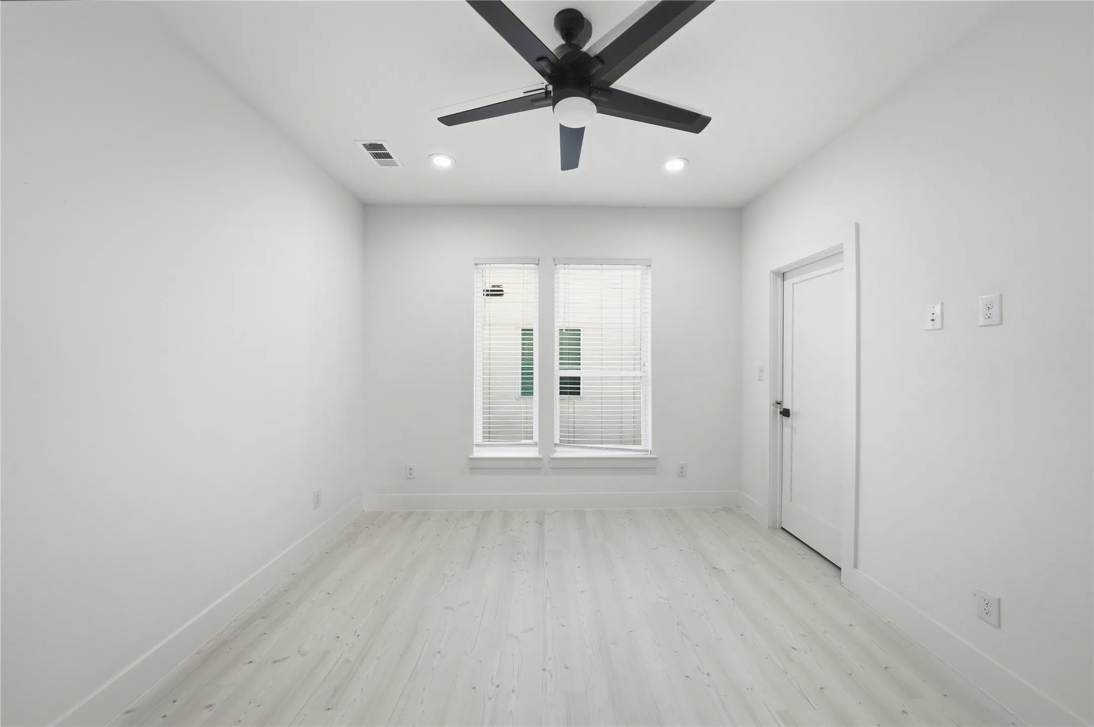 Room with light wood-finish flooring, white walls, and a black ceiling fan with integrated lighting