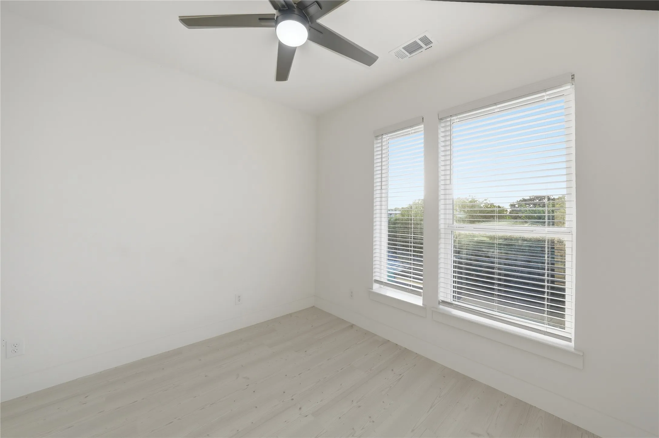 Room featuring two double-hung windows with blinds, wood-finish flooring, and a ceiling fan with integrated lighting