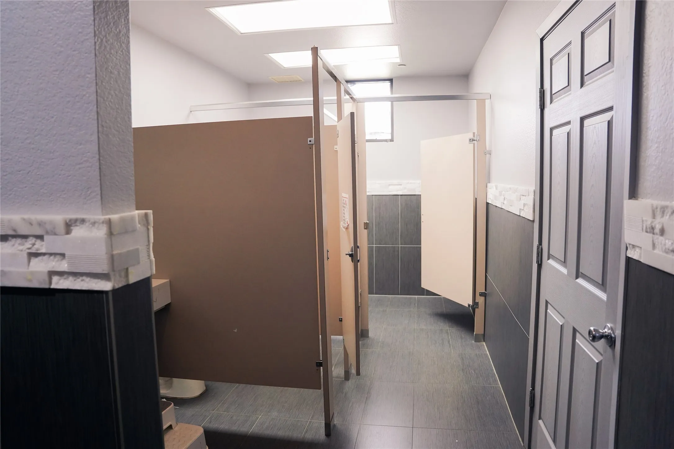 Recessed ceiling lighting, paneled privacy partitions, tiled flooring, and a stone accent wall