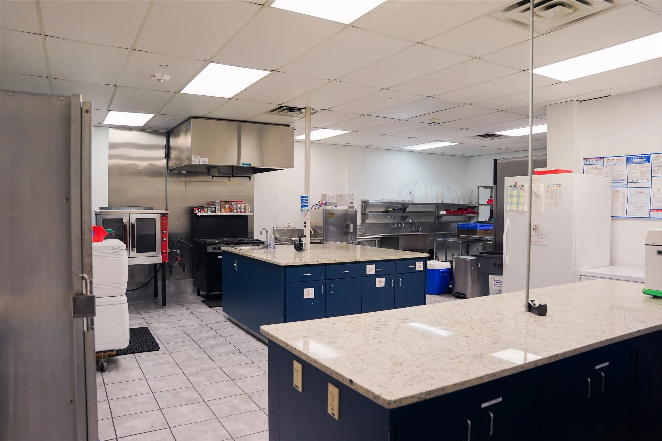 Commercial kitchen featuring two large islands with speckled countertops, stainless steel appliances, and tiled flooring