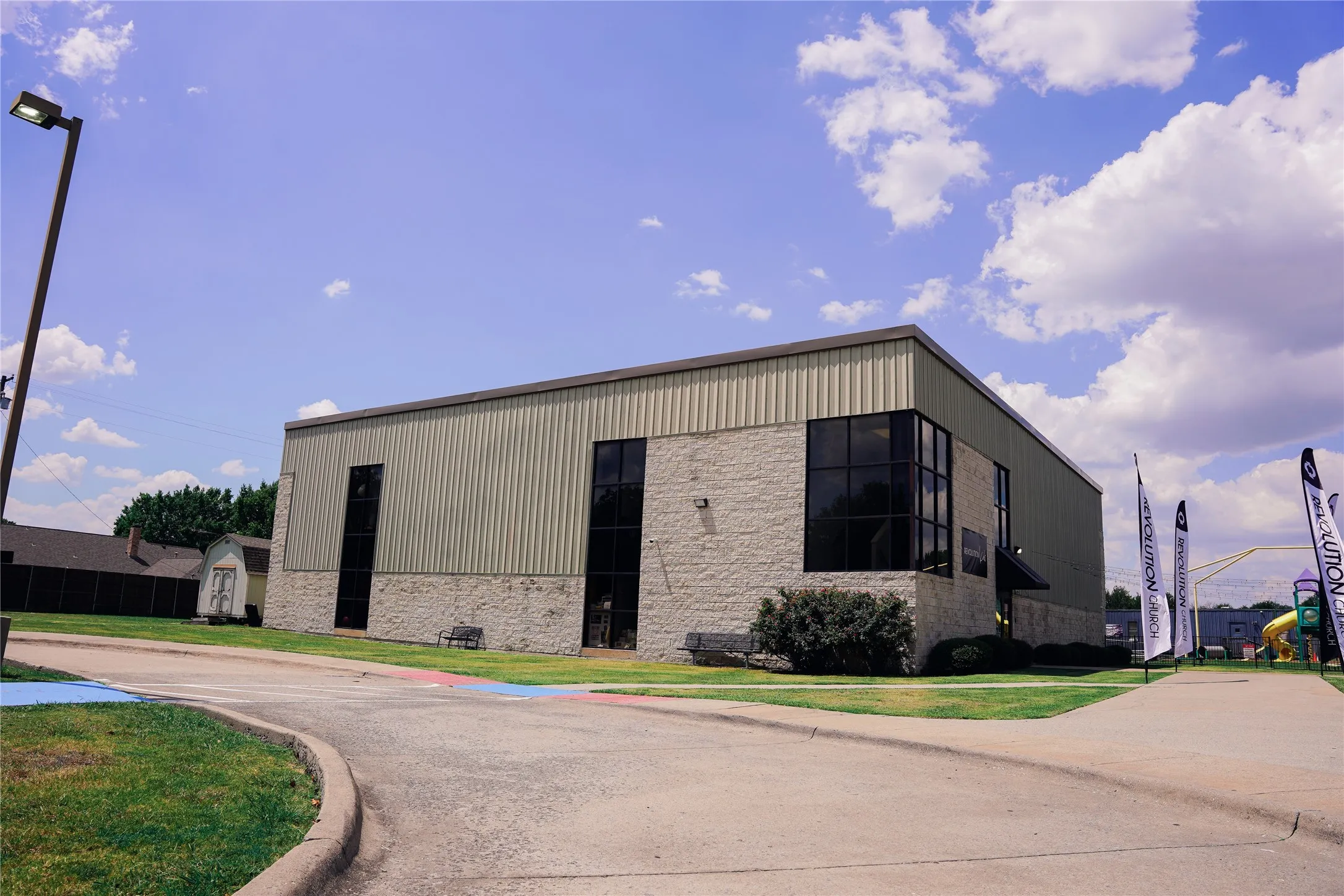 Commercial property featuring a stone and metal exterior, large pane windows, and a paved parking area
